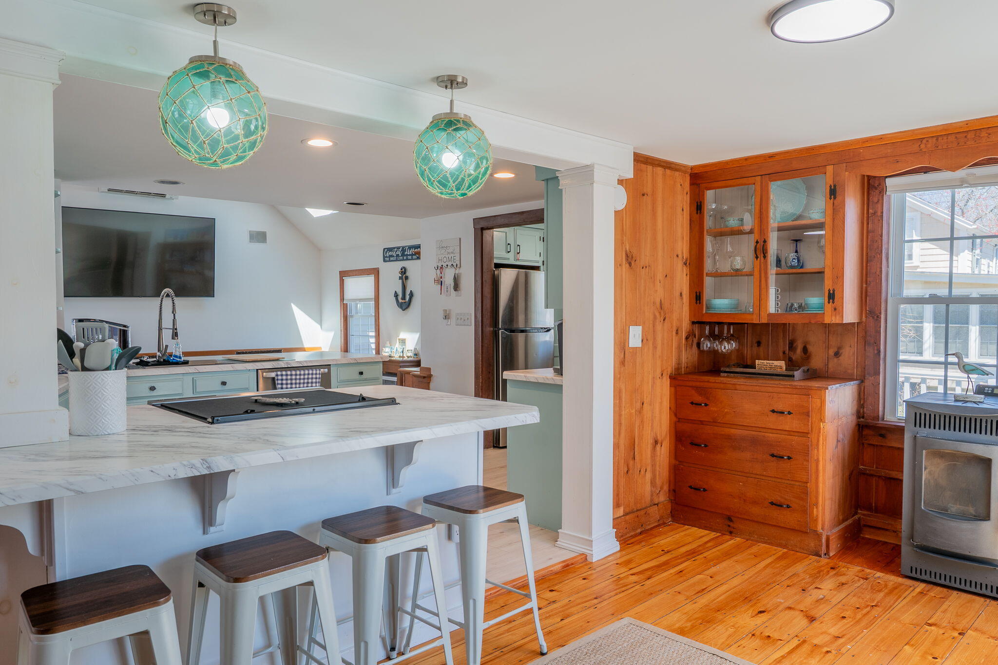 Open kitchen with a marble island and stools beside a wood-paneled dining nook and wood stove.