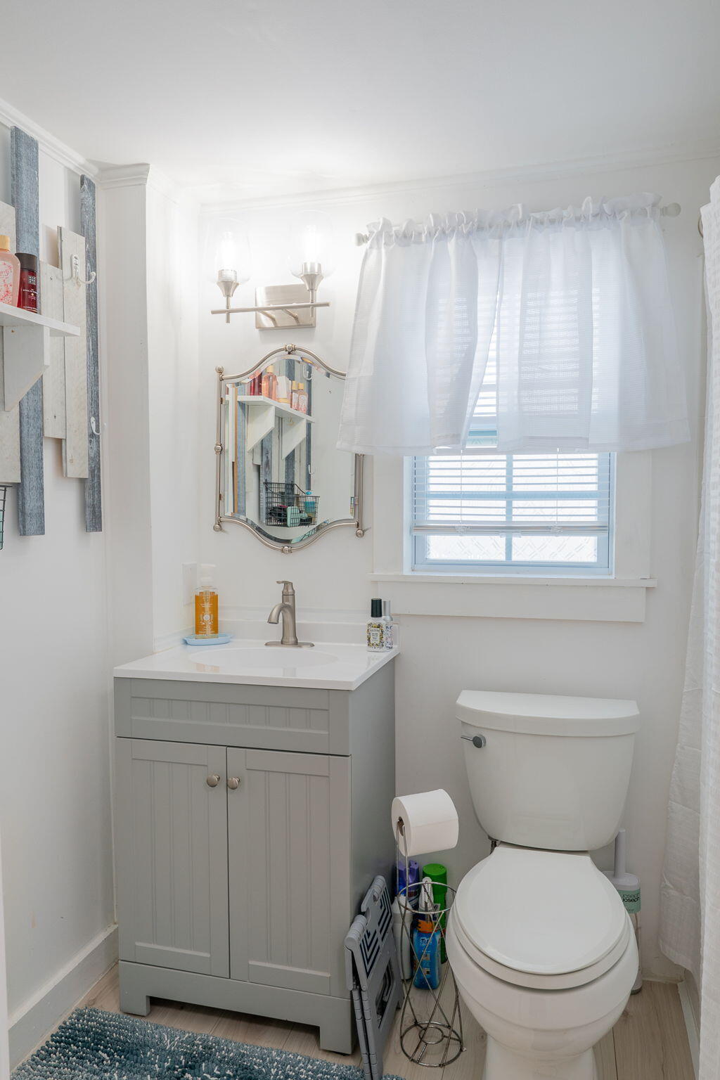 Bathroom with a gray vanity, white toilet, and window with sheer curtains.