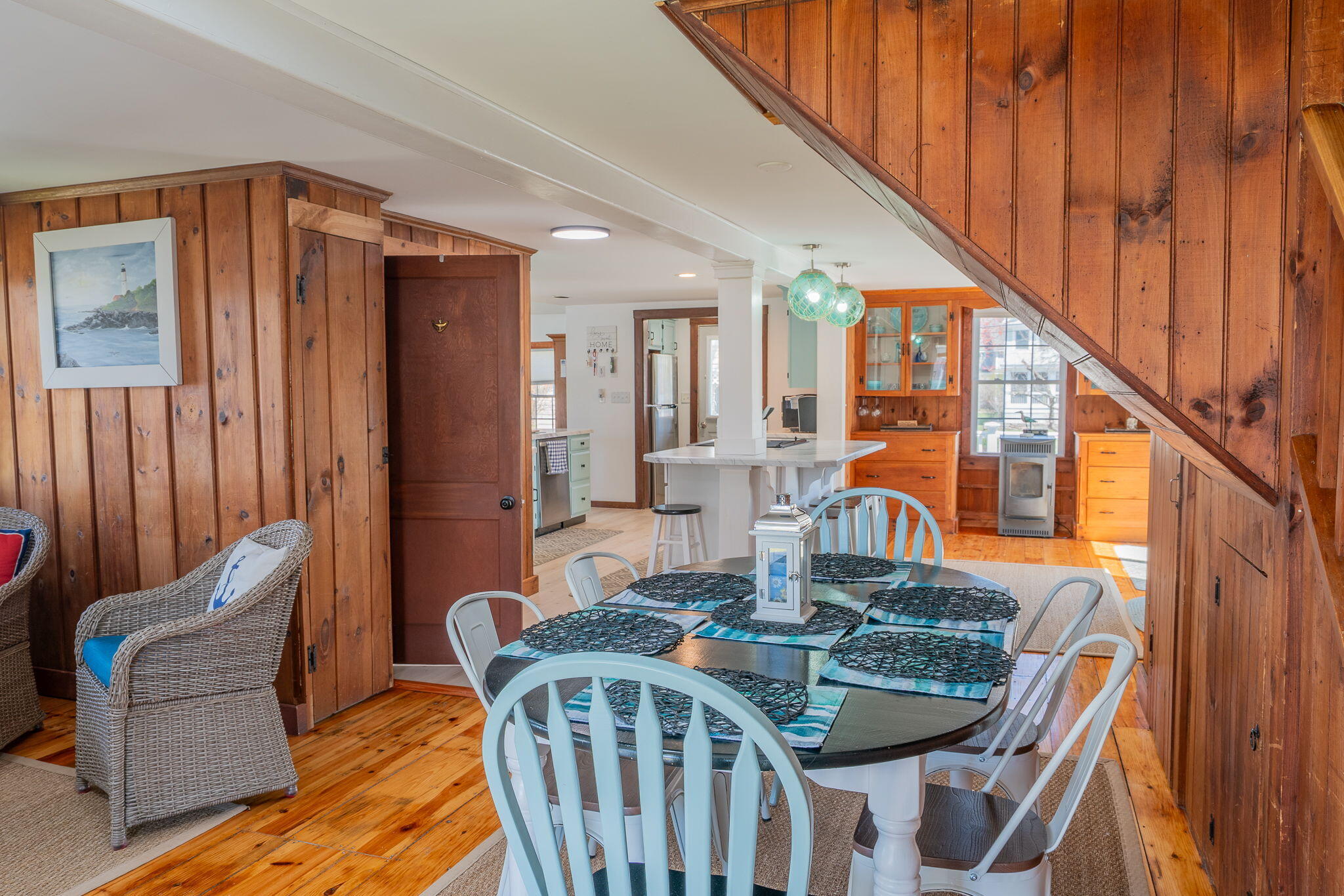 Dining area with wood-paneled walls, a set table, and kitchen island beneath a wooden staircase.