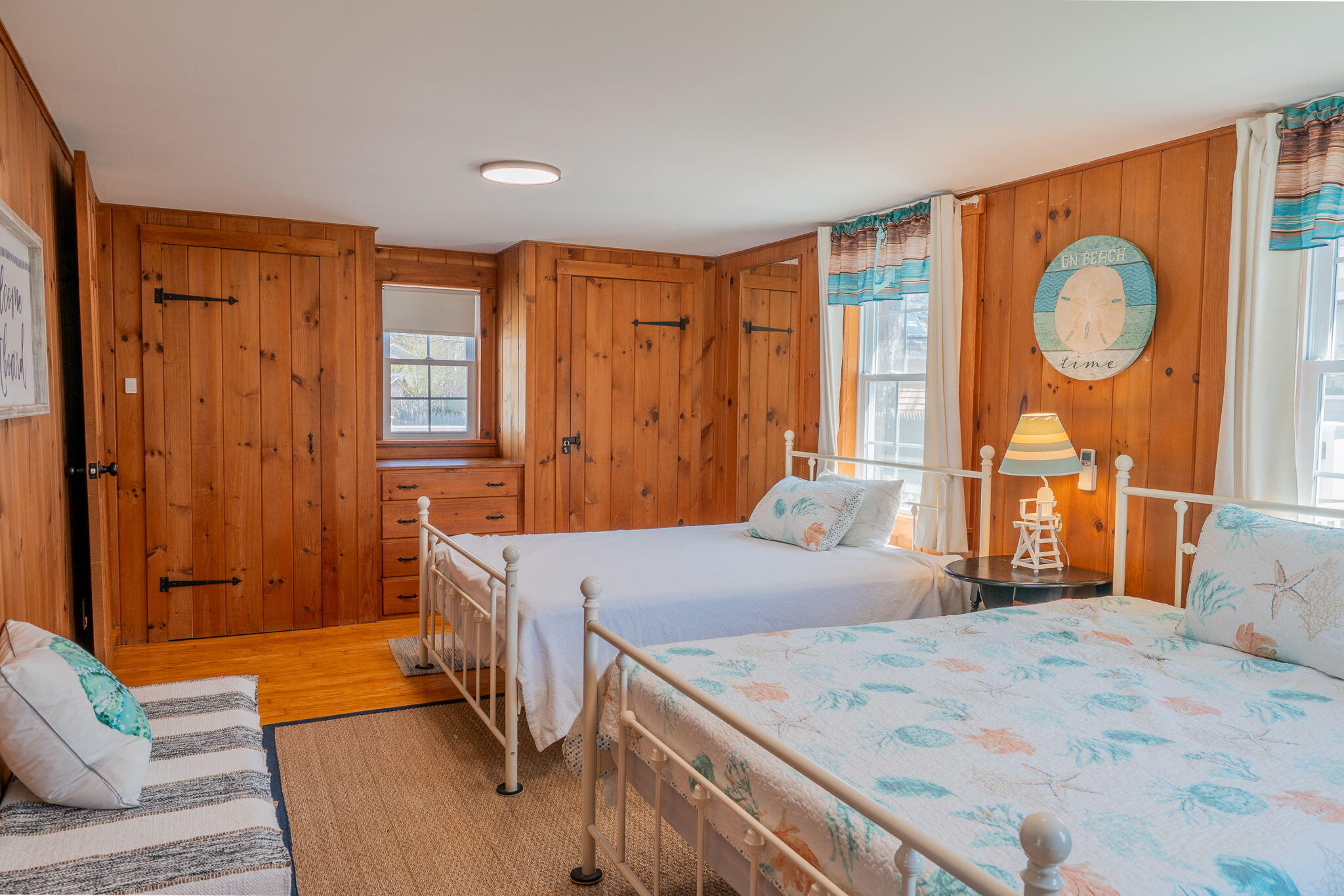 Bedroom with two coastal-print beds, warm wood-paneled walls, and built-in storage.