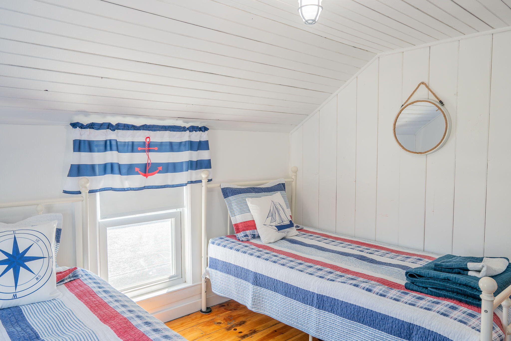 Bedroom with two nautical-themed single beds, white paneled walls, a sloped ceiling, and wood flooring.