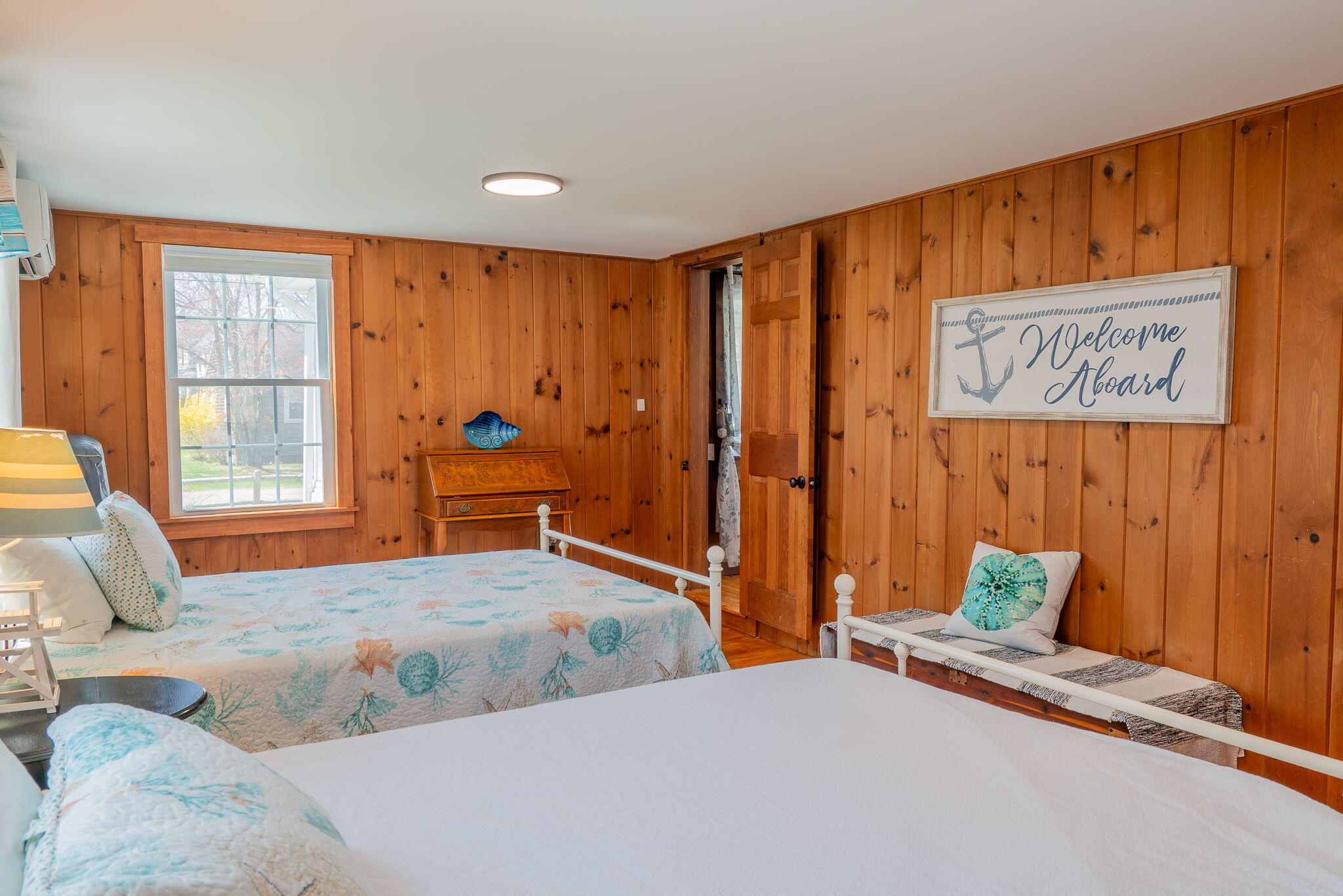 Bedroom with wood-paneled walls, two beds with nautical bedding, and a framed “Welcome Aboard” sign.