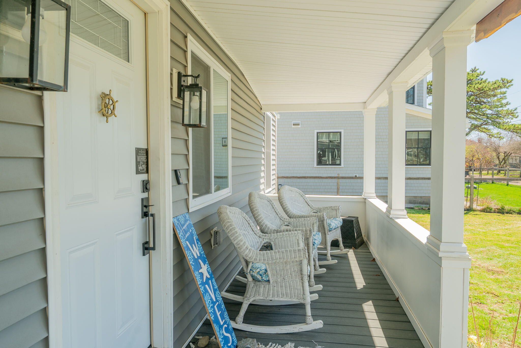 Covered front porch with white wicker rockers, blue cushions, and a view of the lawn.