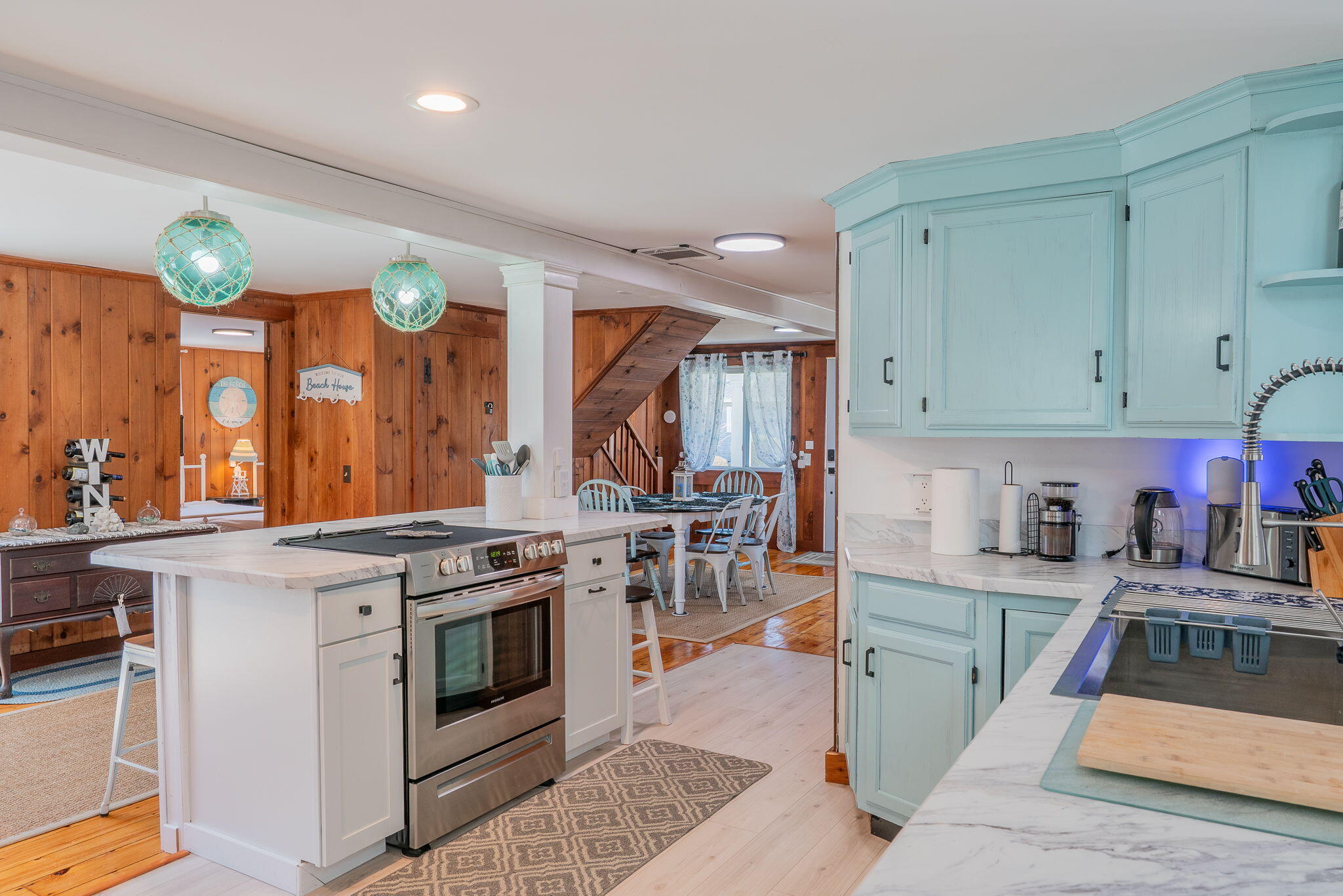 Open-plan kitchen with pale aqua cabinets, marble counters, and a stainless-steel range in the island.