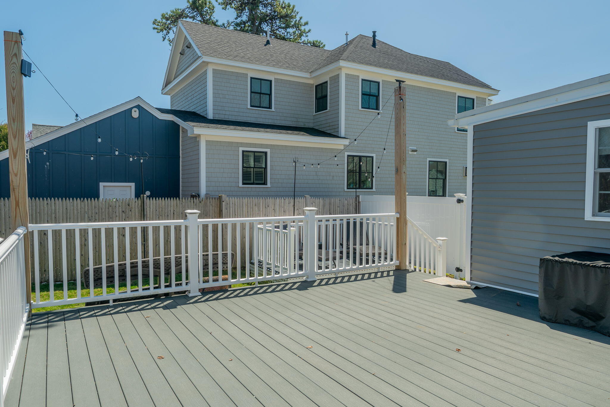 Spacious gray deck with white railings, string lights, and a fenced yard behind the house.