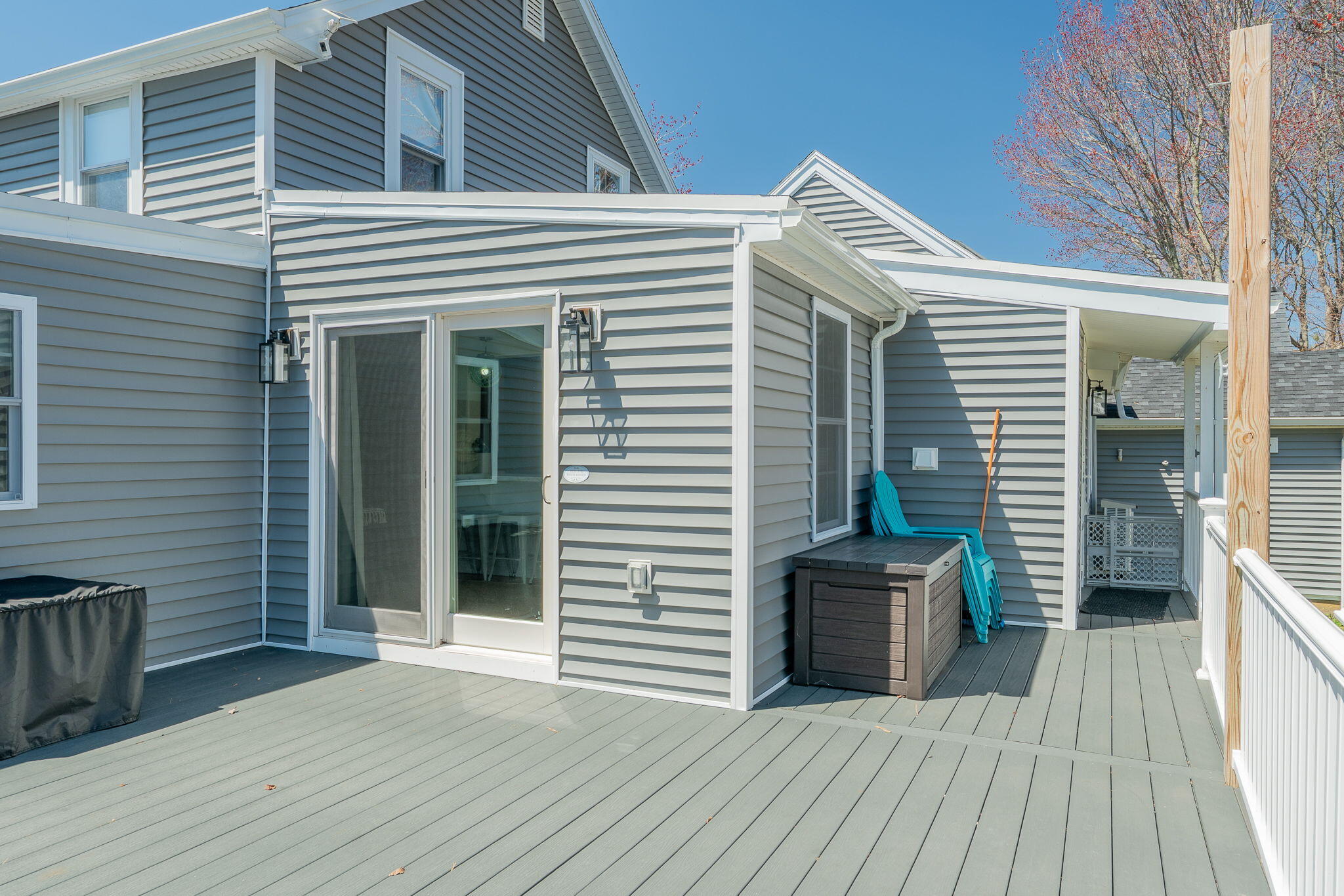 Wide gray deck beside a gray-sided house, with turquoise chairs and a covered passageway.