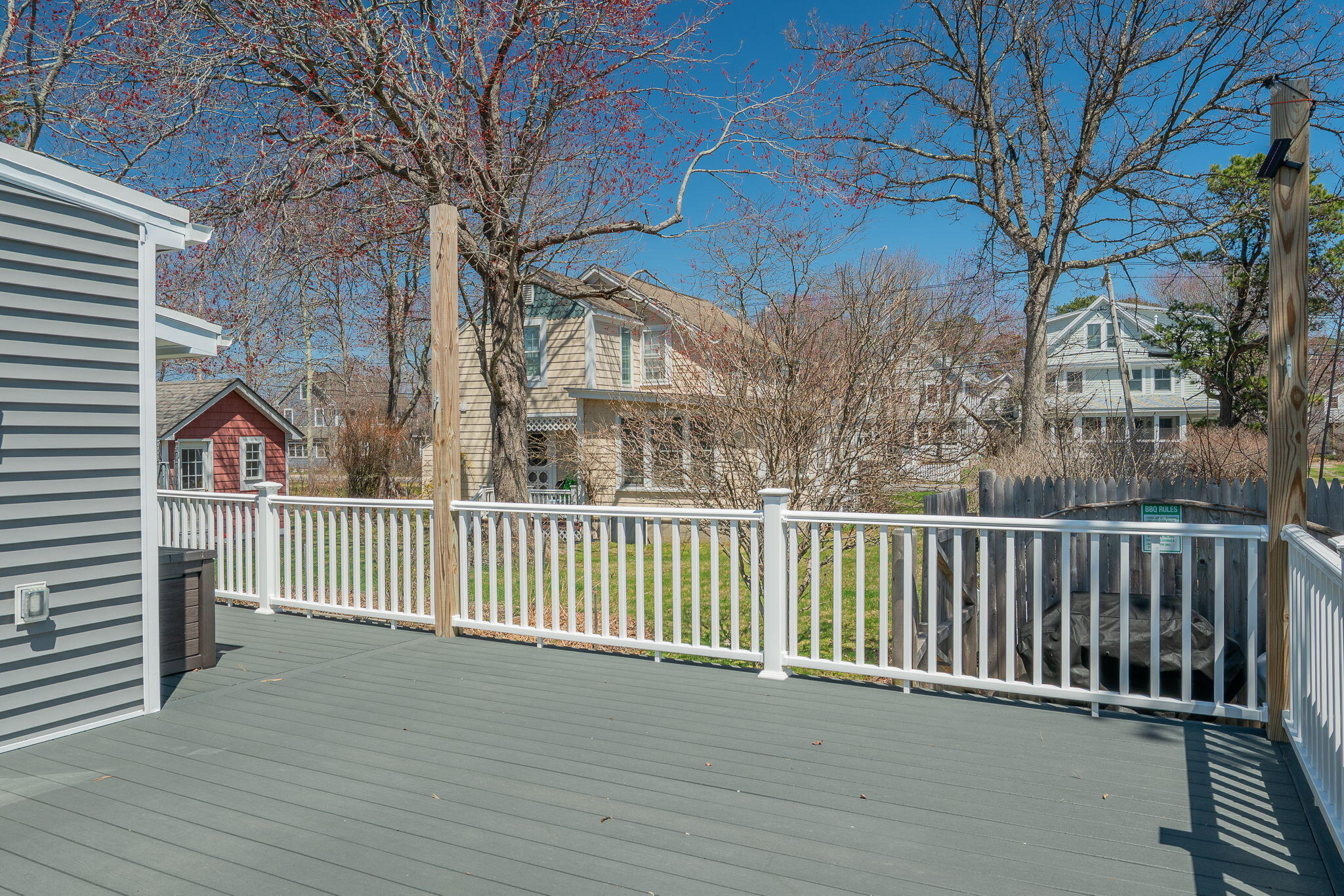 Gray deck with white railings overlooking a fenced yard and neighboring homes.