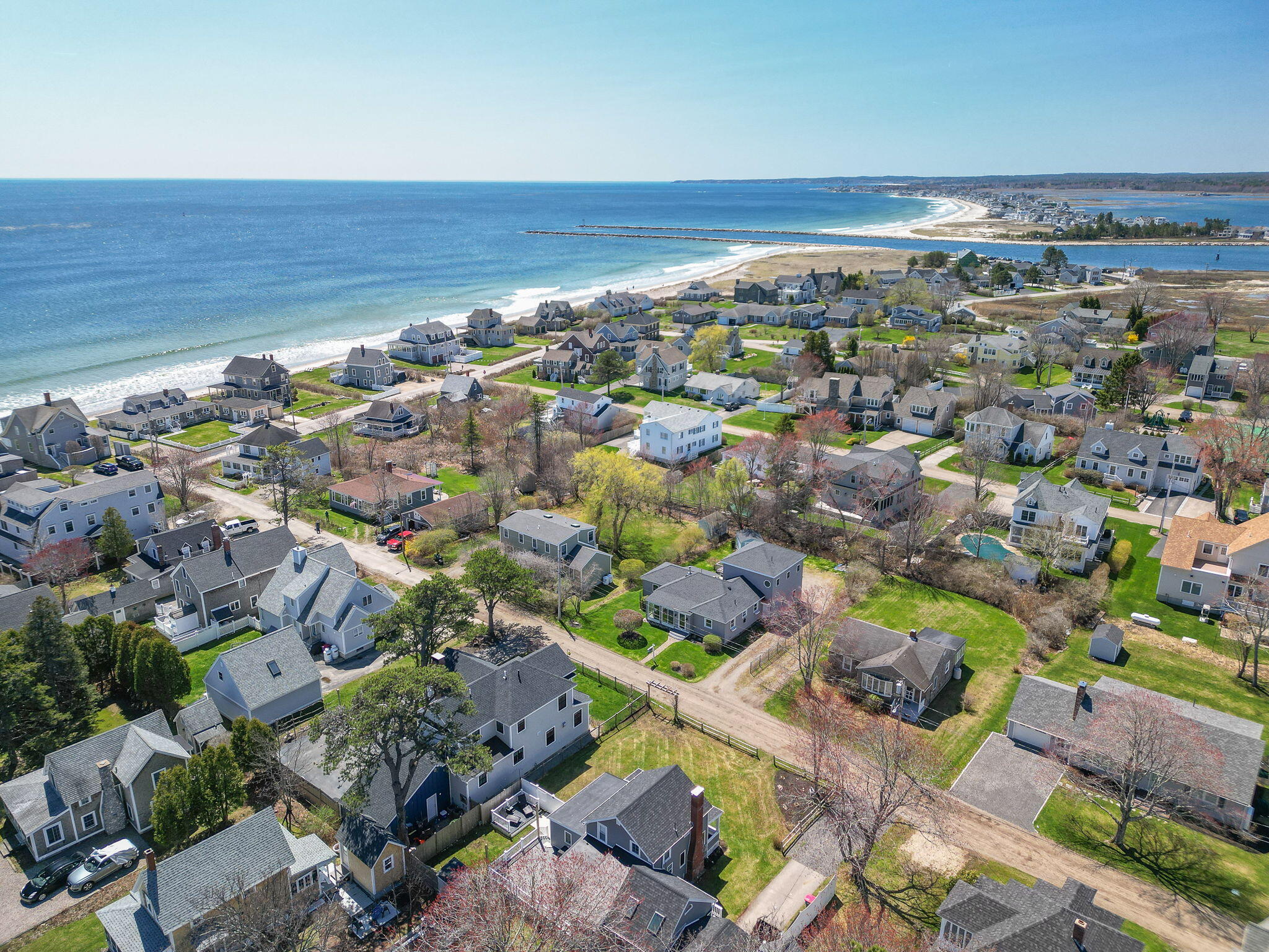 Aerial view of a coastal neighborhood with homes, sandy beach, ocean, and inlet.