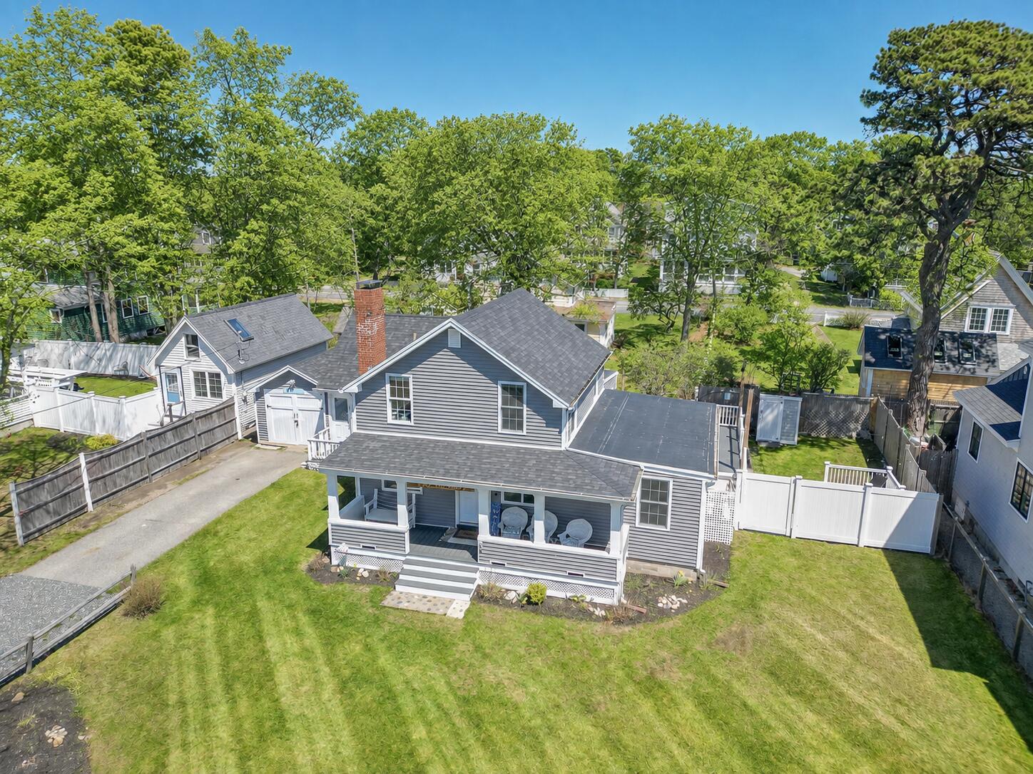 Aerial view of a gray house with a covered porch and fenced lawn.