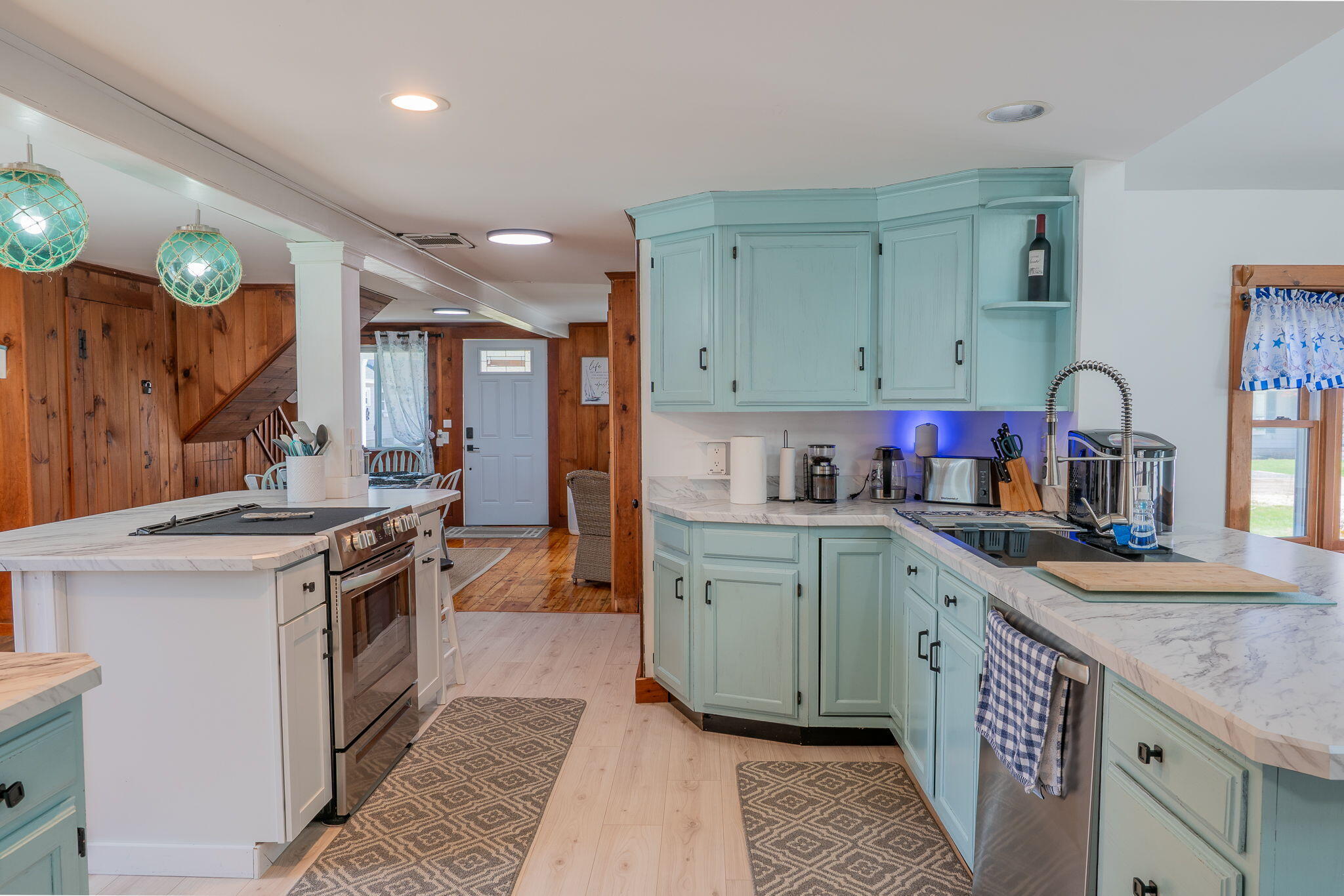 Kitchen with pale aqua cabinets, marble-look counters, a large cooktop island, and turquoise pendant lights.