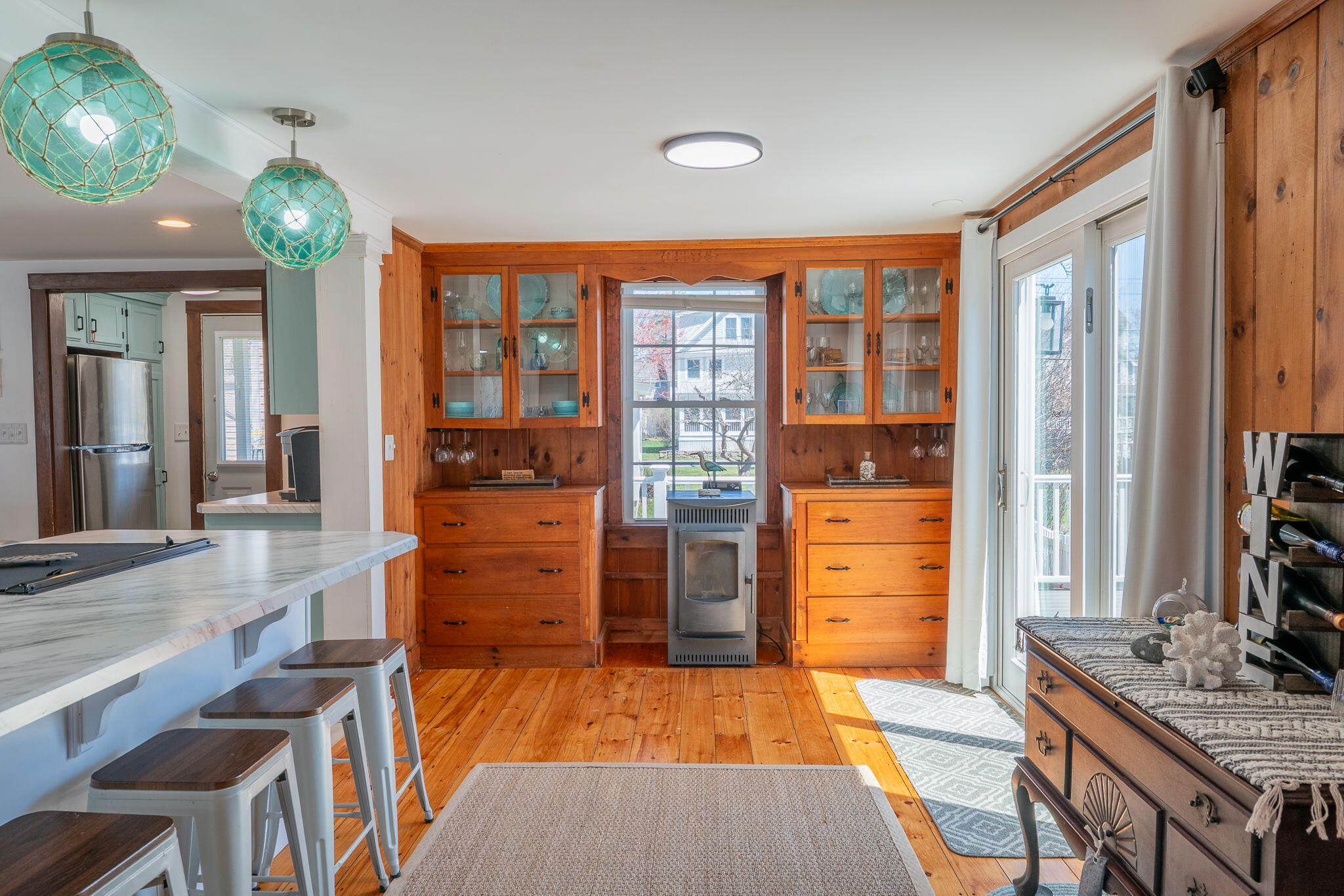 Dining area with pine built-ins around a window, a compact stove, and a marble-look island with stools.