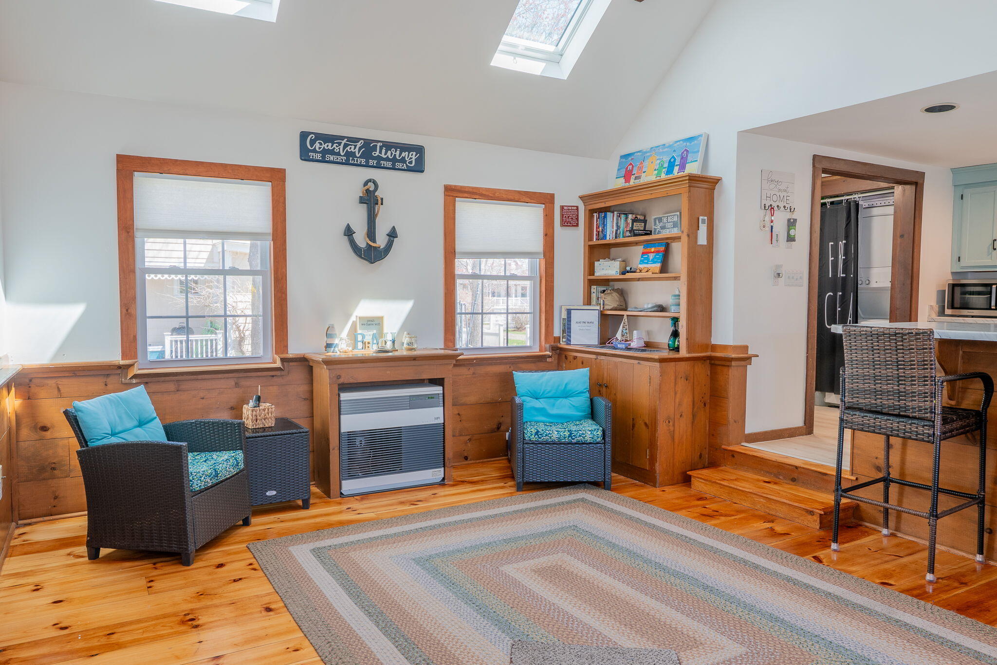 Furnished sitting room with turquoise-cushioned wicker chairs, wood floors, built-in bookcase, and skylights.