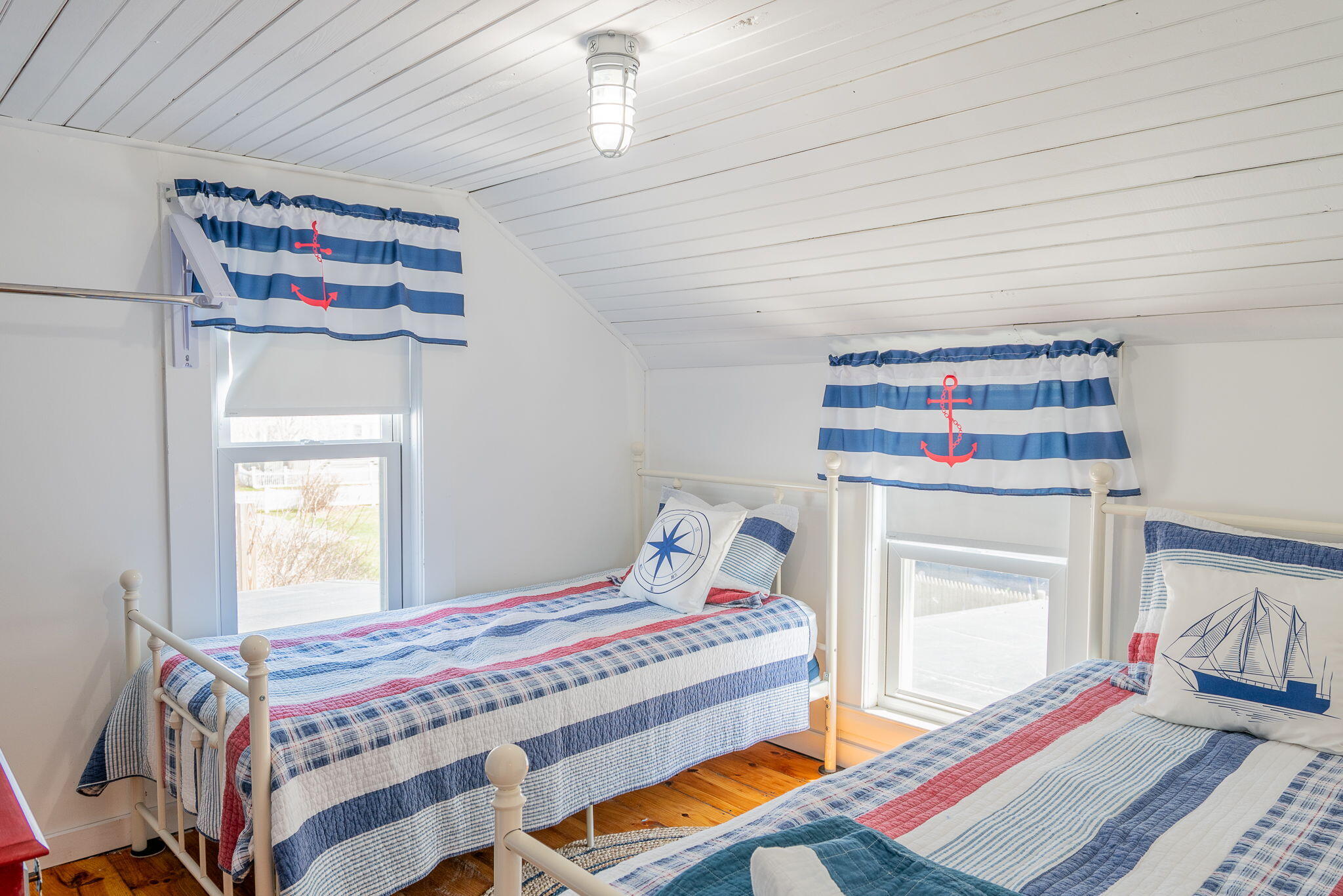 Bedroom with two twin beds dressed in blue and red nautical quilts and anchor curtains.