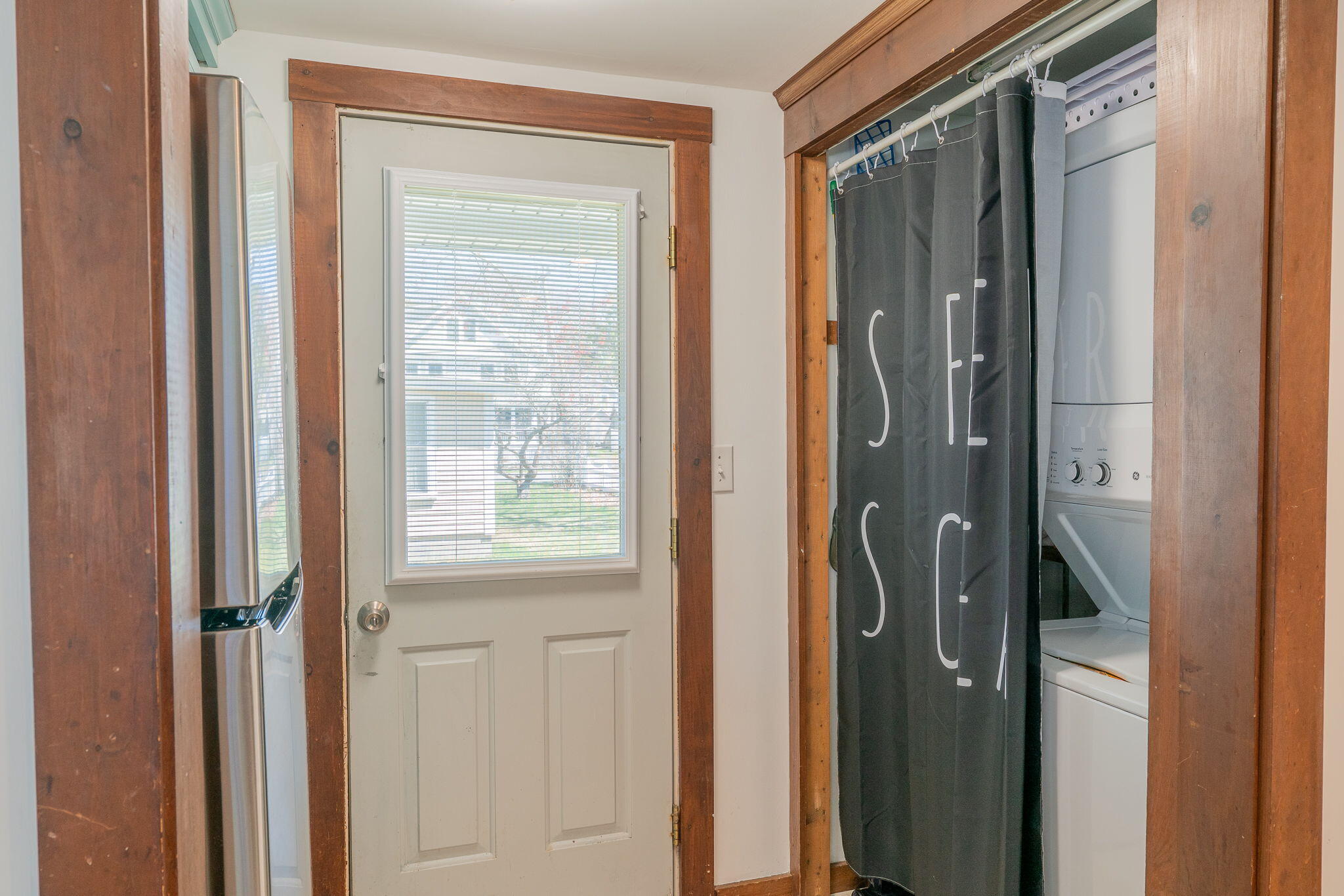 Laundry area with a stacked washer and dryer behind a curtain beside a windowed door.
