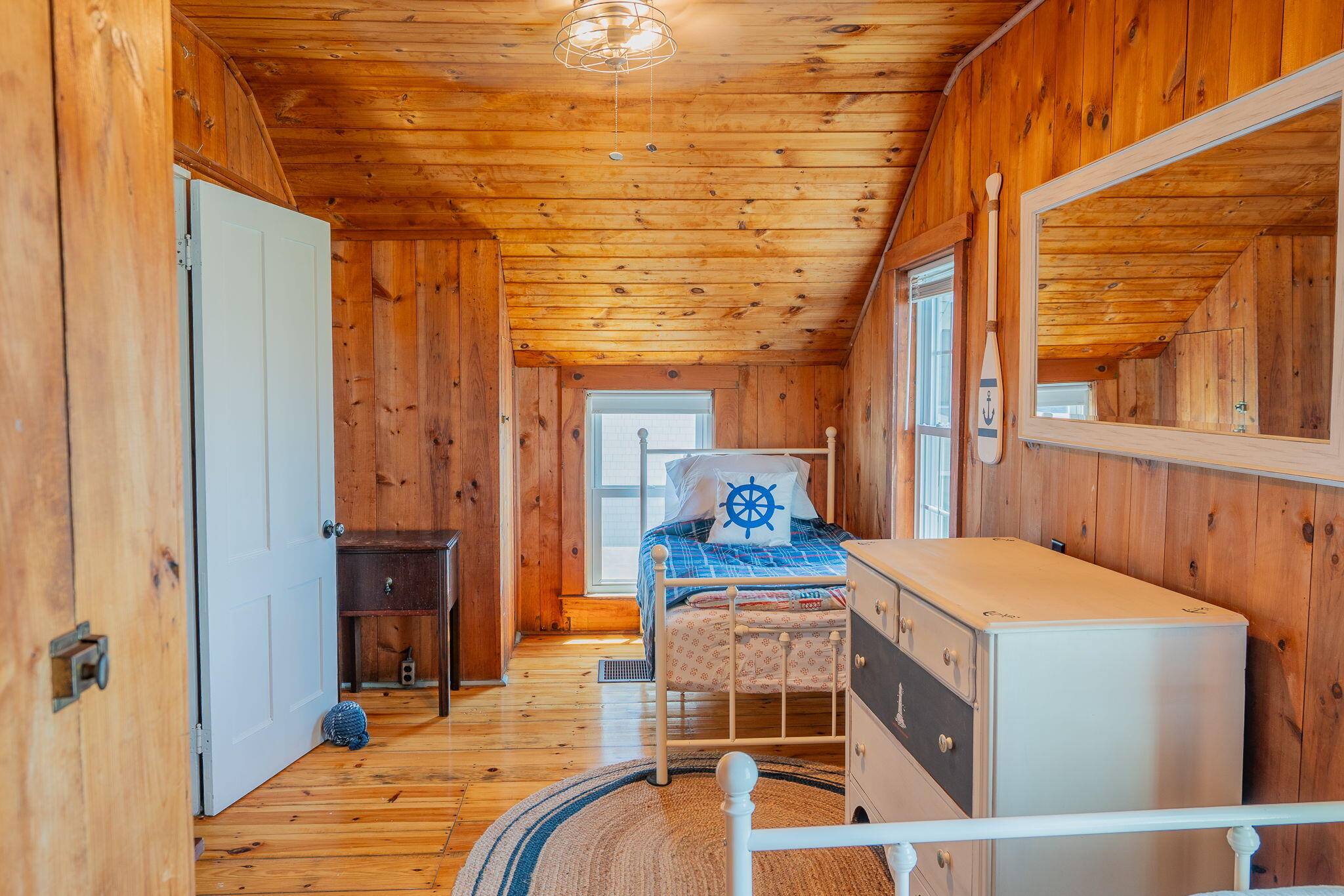 Pine-paneled bedroom with a twin bed, blue plaid bedding, nautical decor, and white dresser.