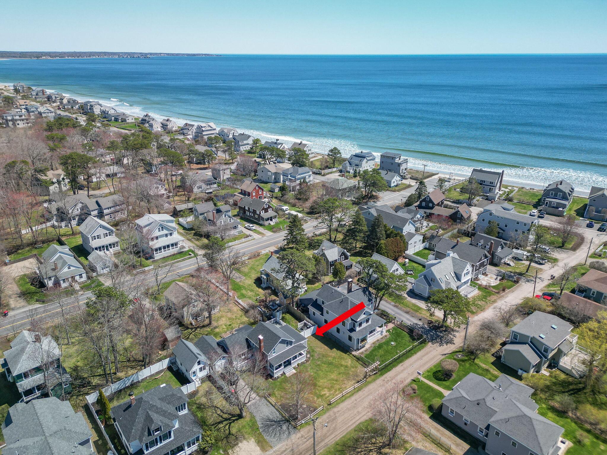 Aerial view of the coastal neighborhood, with a red arrow pointing to the featured house near the ocean.