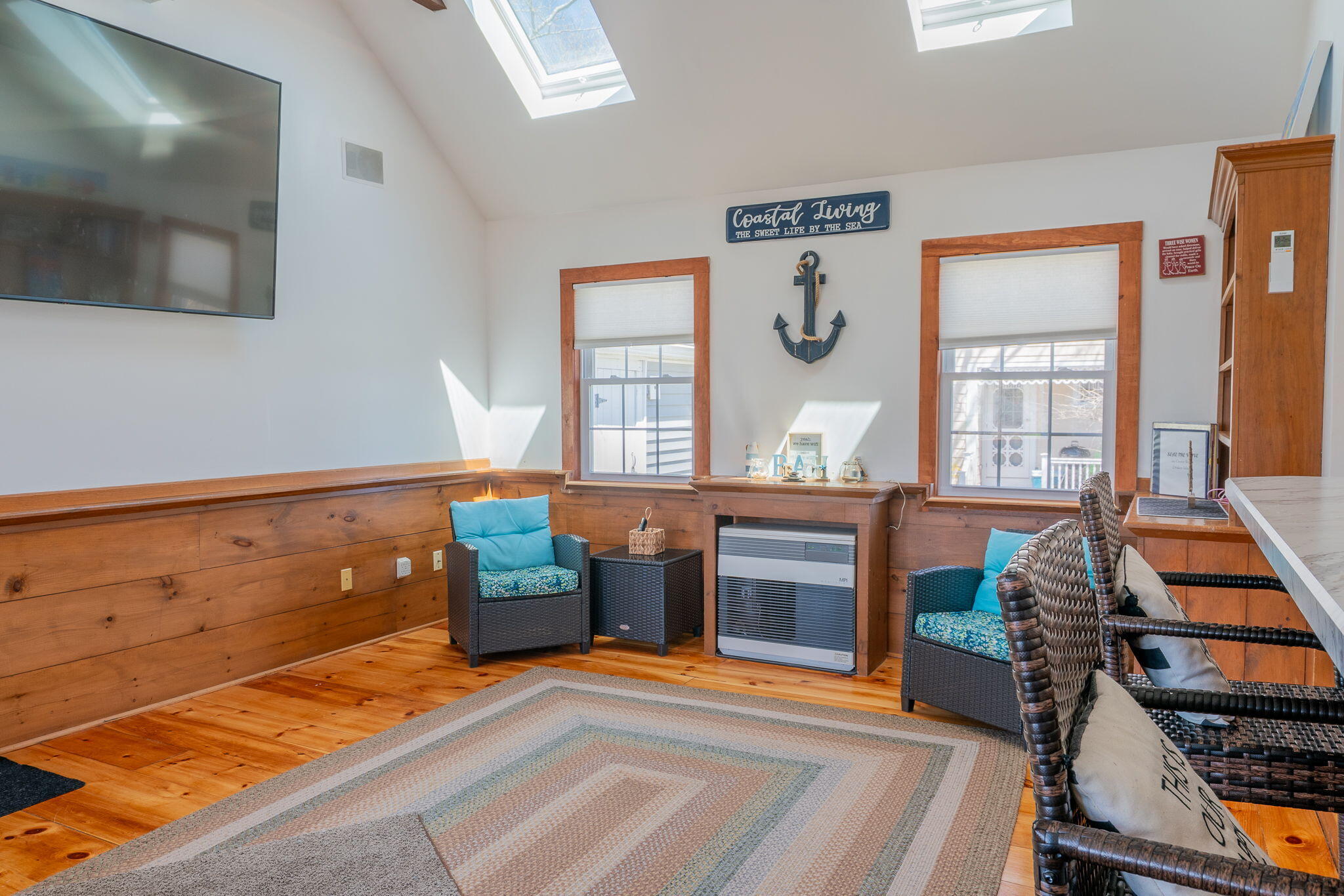 Sunroom with skylights, wicker seating, turquoise cushions, and warm wood flooring.