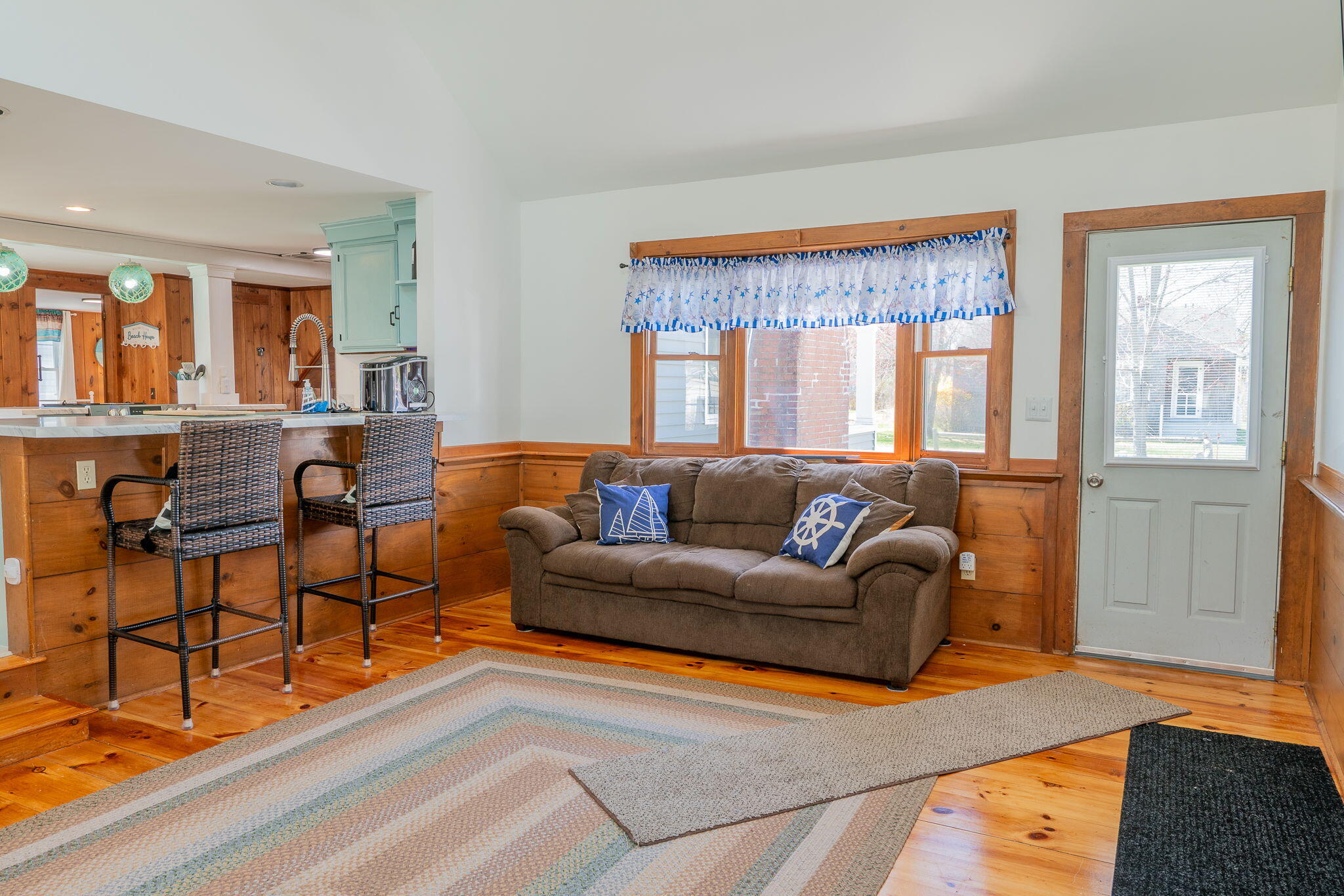 Living room with wood paneling, brown sofa, hardwood floors, and an open kitchen breakfast bar.