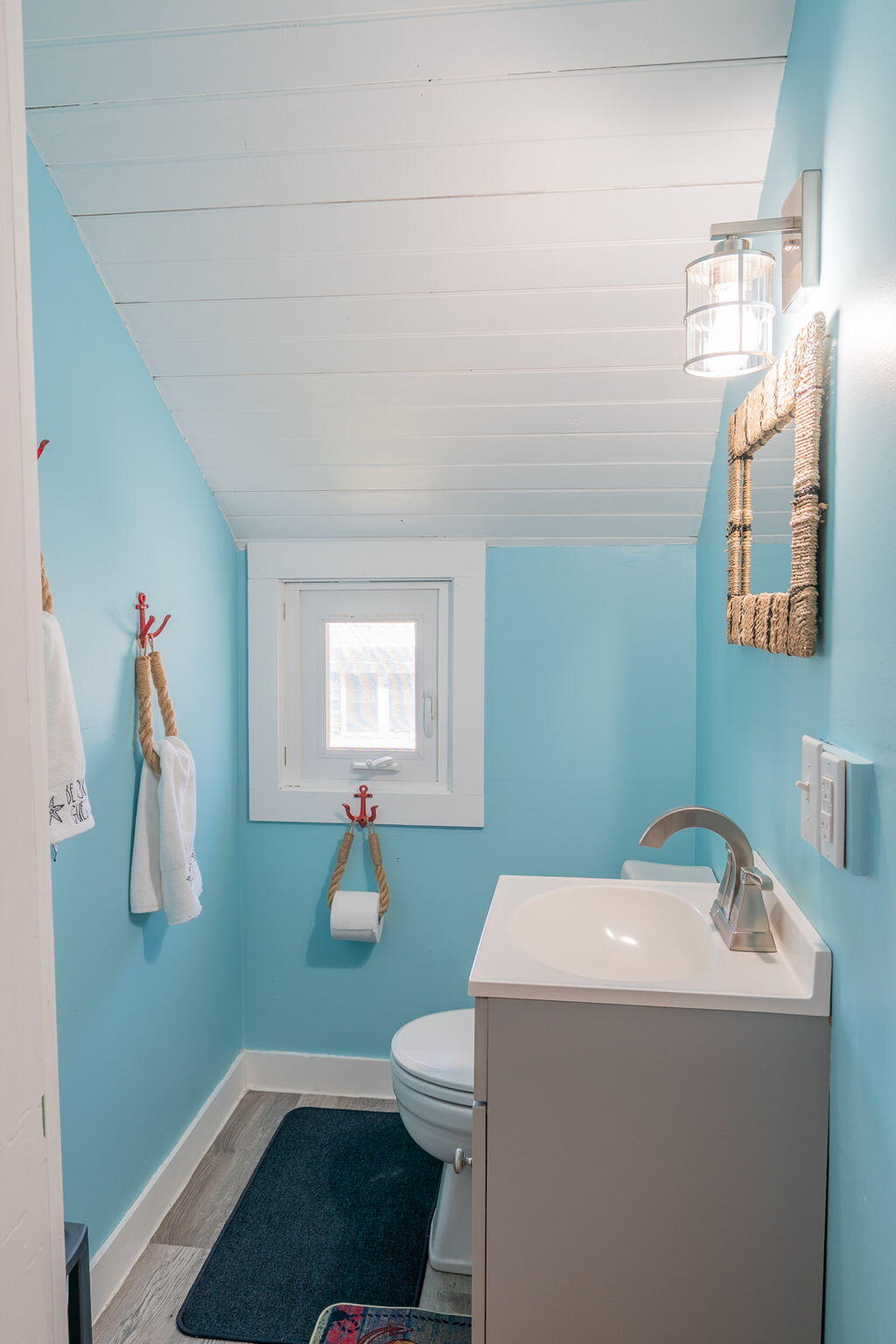 Turquoise bathroom with a gray vanity, small window, and sloped white plank ceiling.