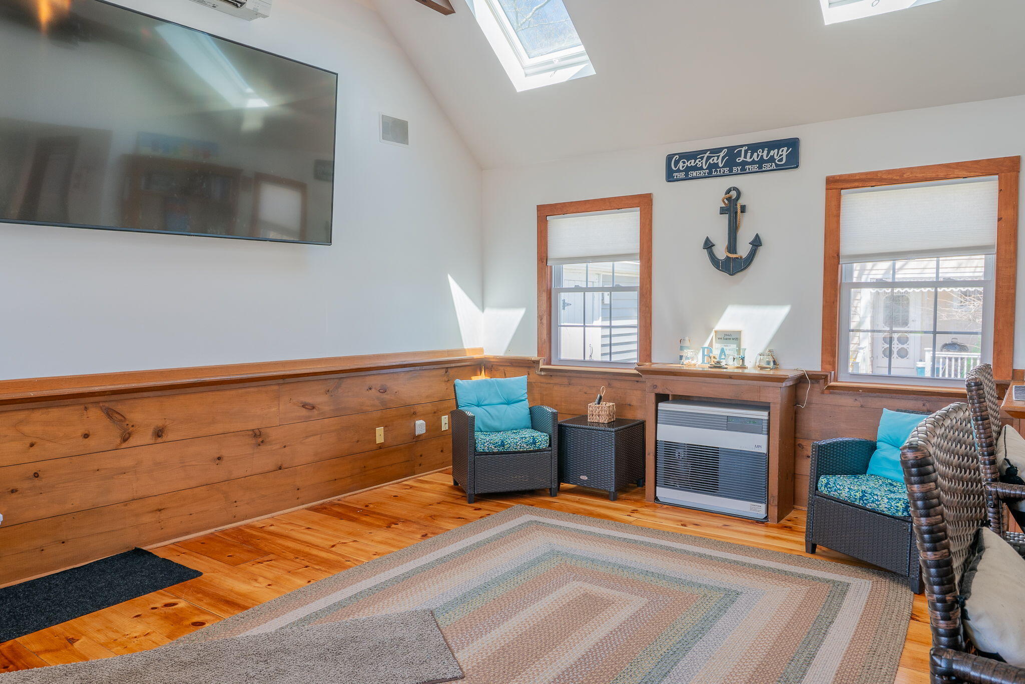 Coastal-style sitting room with wood wainscoting, turquoise-cushioned wicker chairs, and skylights.