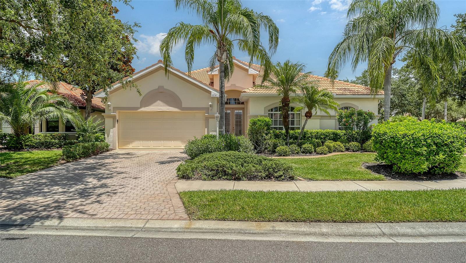 Cream stucco home with terracotta tile roof, palm trees, and curved paver driveway