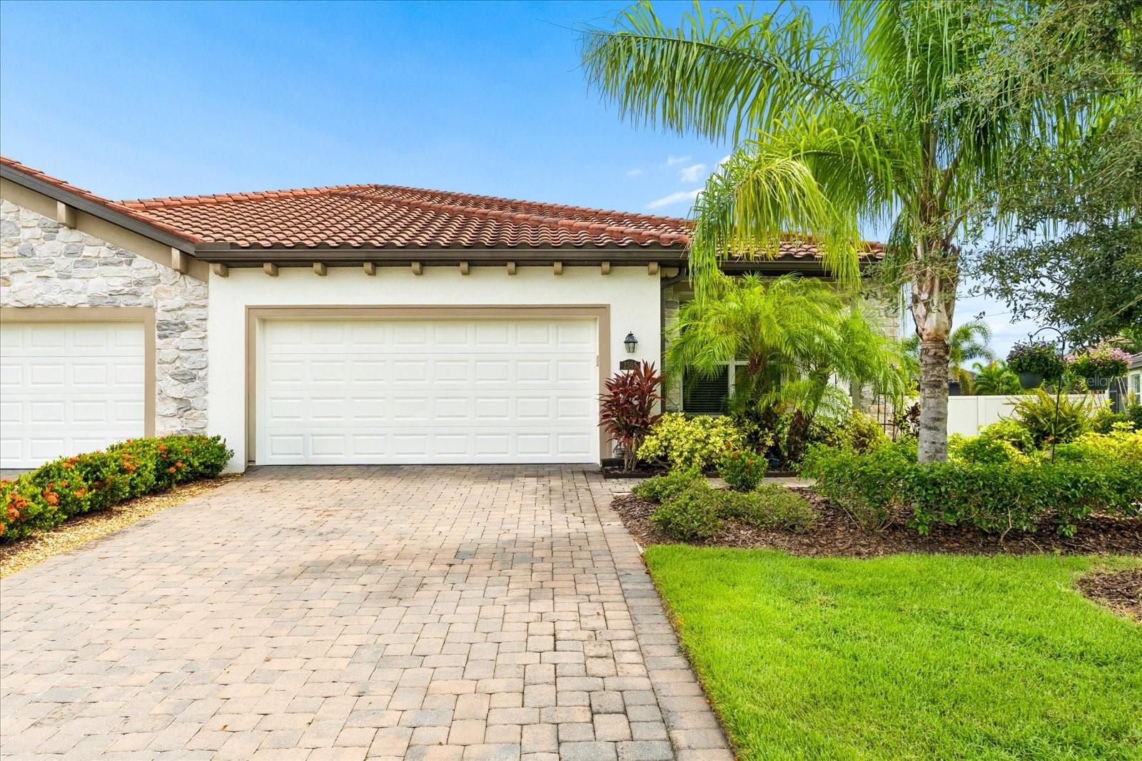 Home with a terracotta tile roof, stone accents, two garage doors, and a landscaped paver driveway.