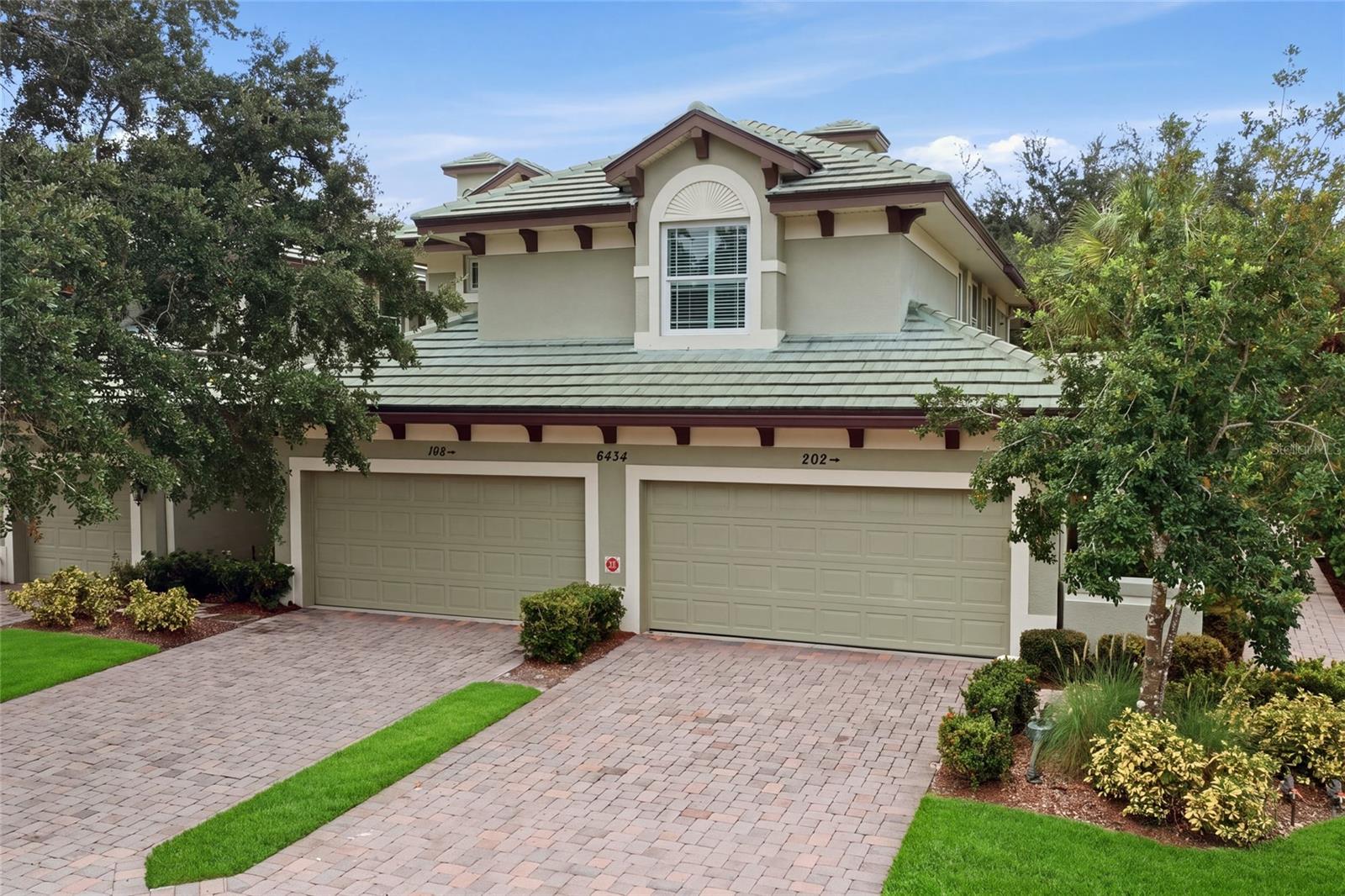 Building exterior with two garage doors, green tile roof, and brick-paver driveways.
