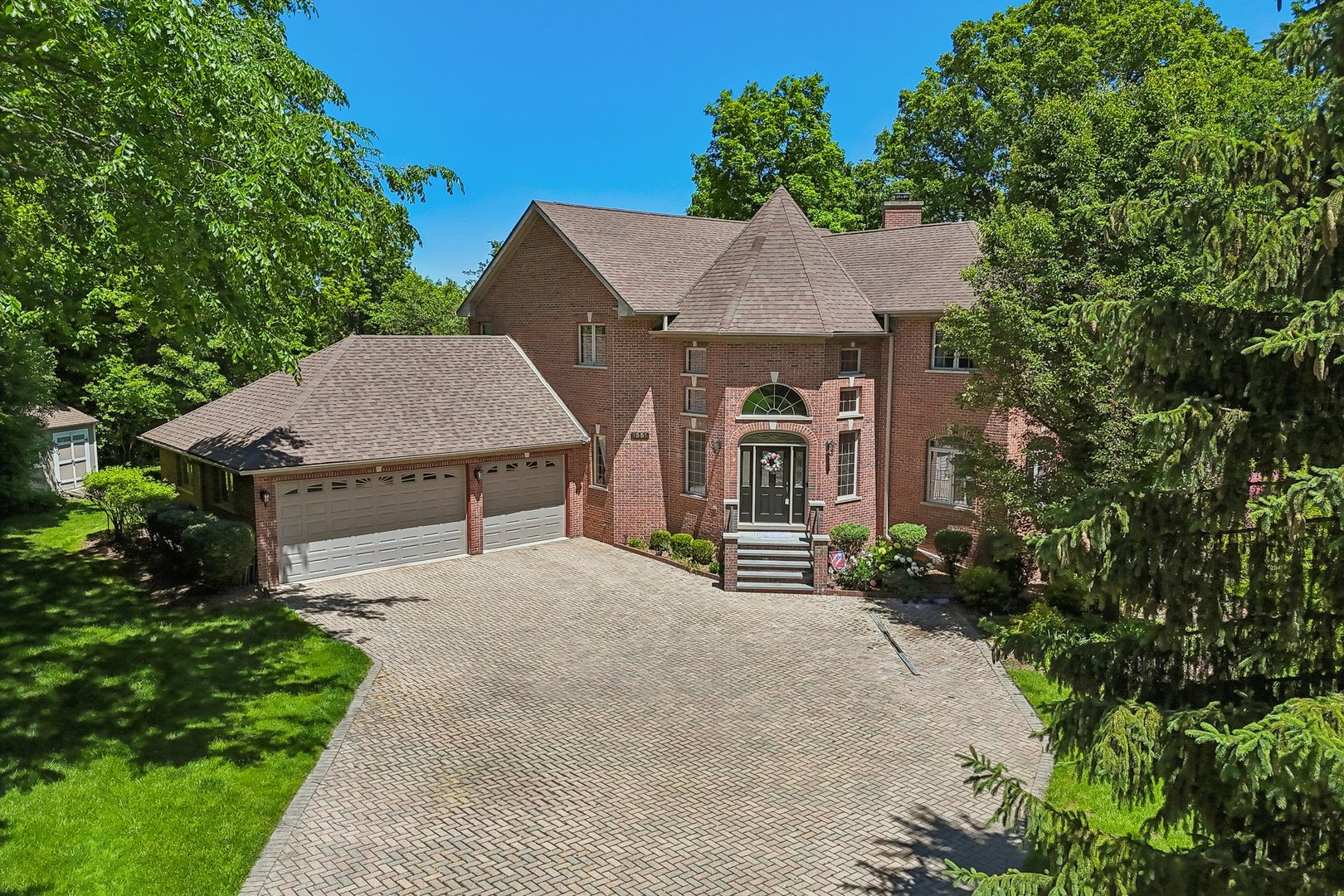 Two-story red-brick home with an arched entrance, attached garage, and wide brick driveway.