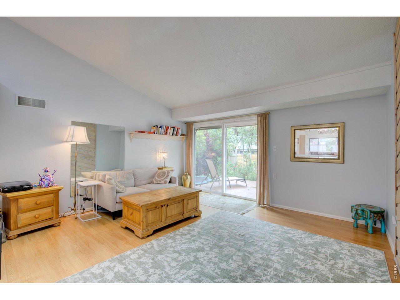 Furnished living room with a high sloped ceiling and sliding glass doors overlooking greenery.