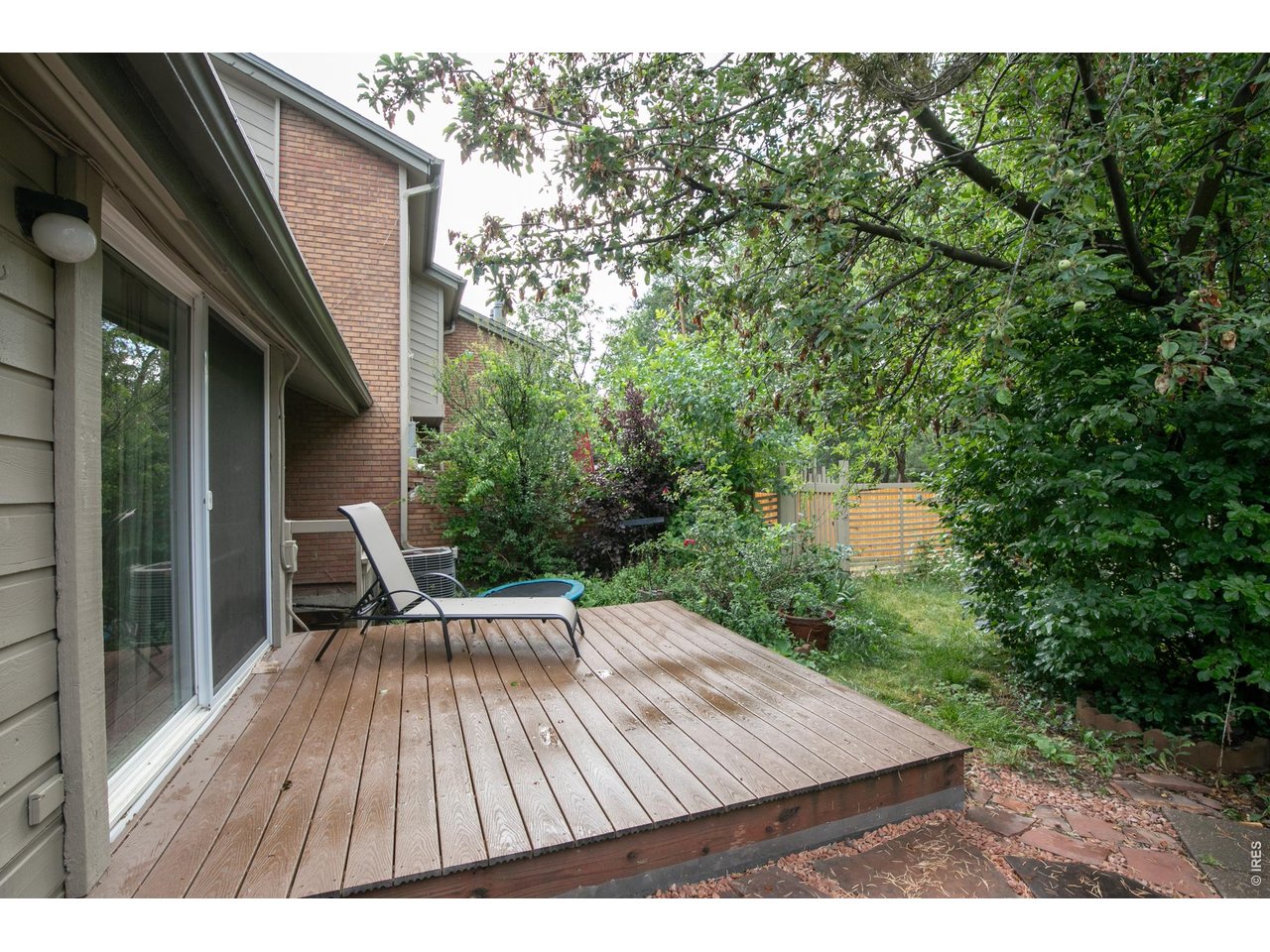 Wooden backyard deck with a lounge chair, sliding glass doors, and a leafy garden.