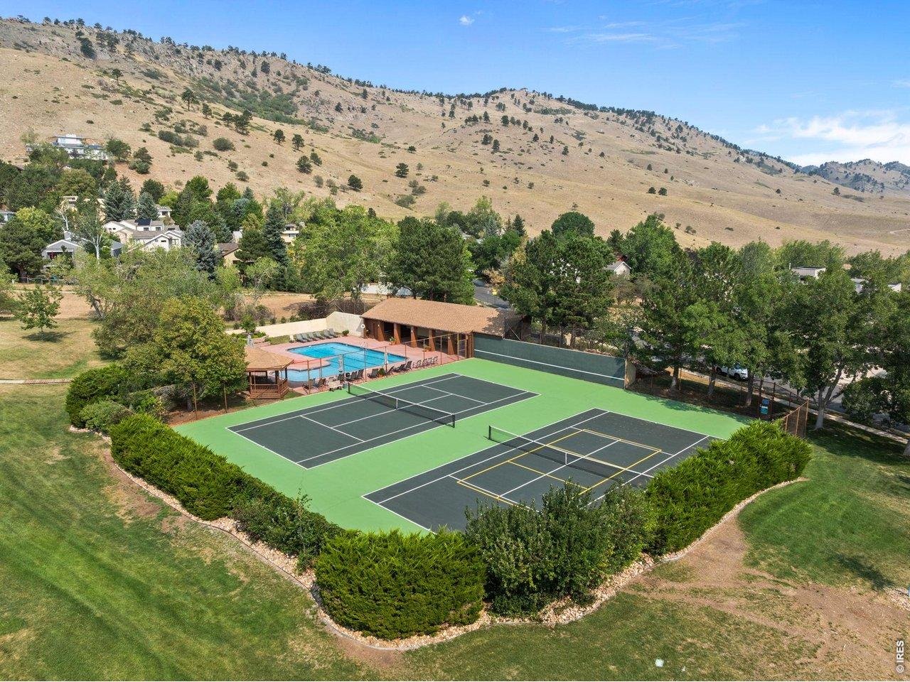 Aerial view of tennis and pickleball courts, a pool, and clubhouse below a Boulder hillside.