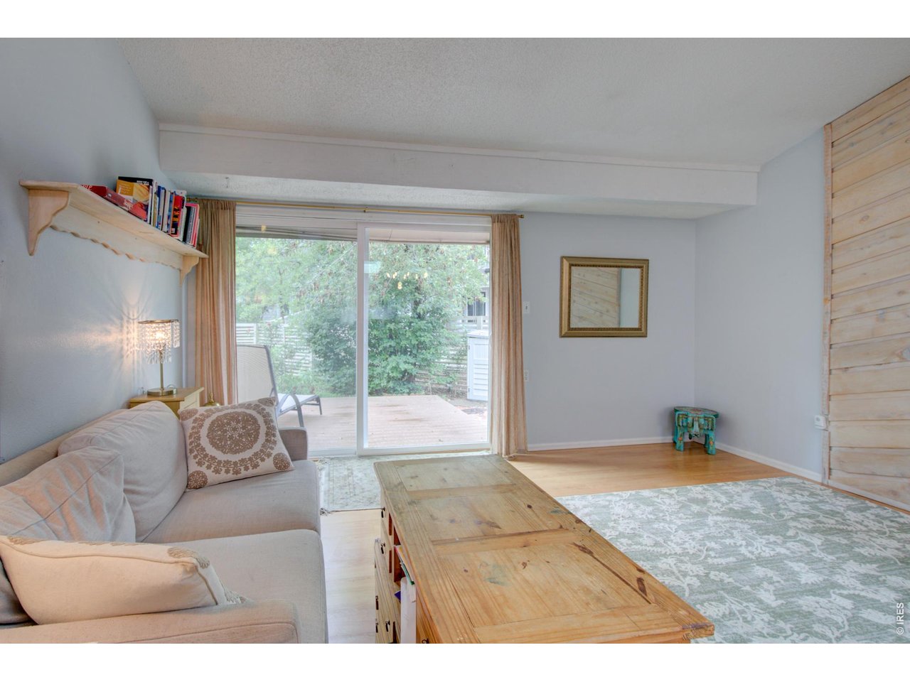 Living room with a pale sofa, wooden coffee table, and sliding doors opening onto a leafy deck.
