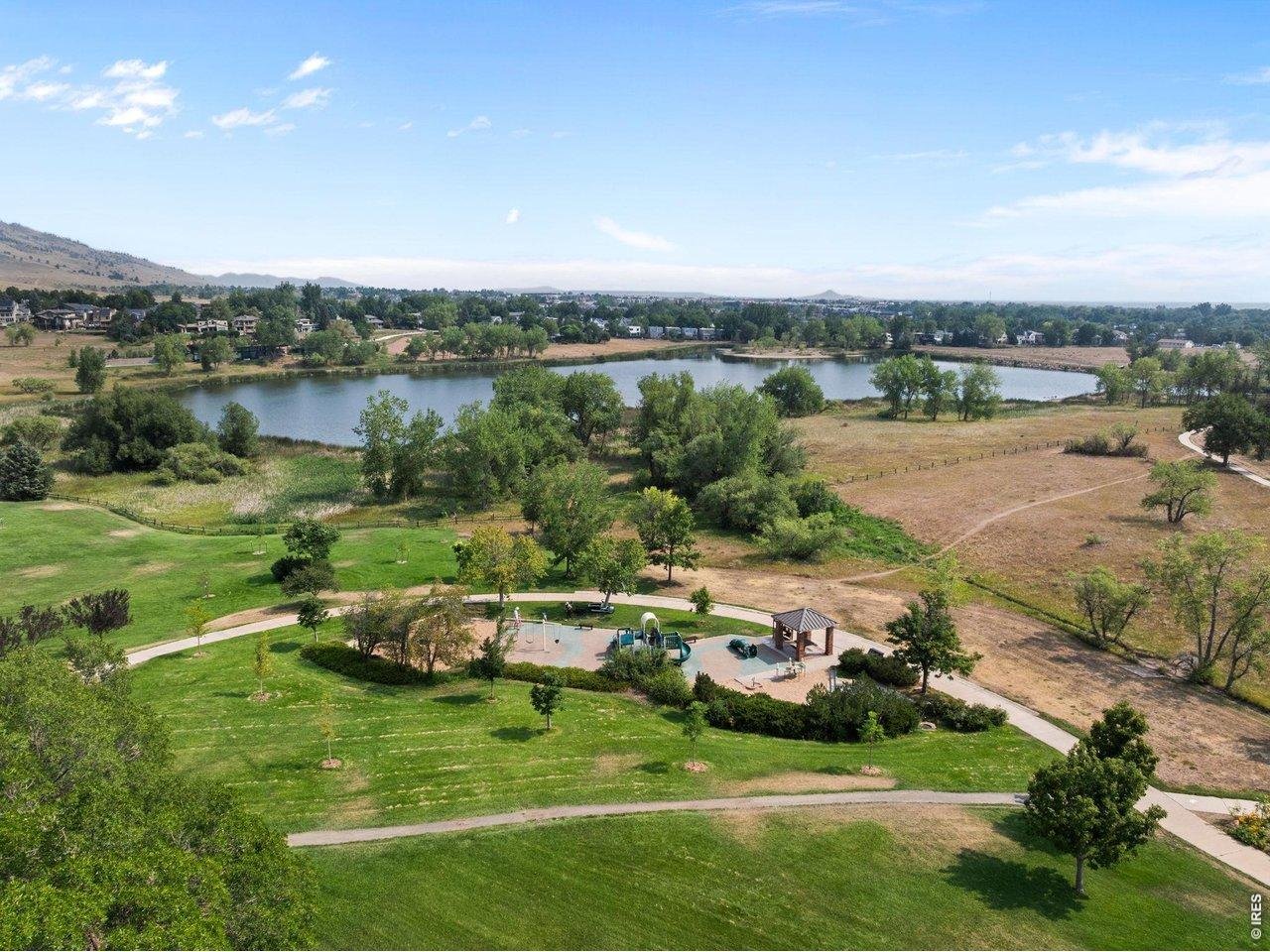 Aerial view of a neighborhood park with a pond, playground, walking paths, and foothills.