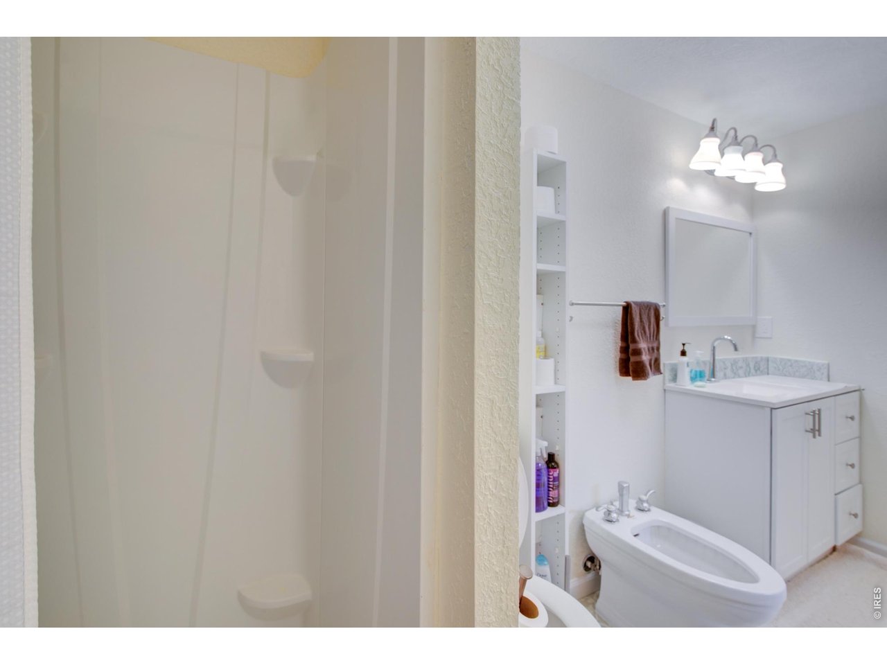 Bathroom with glass shower, open shelving, white vanity, and soaking tub.