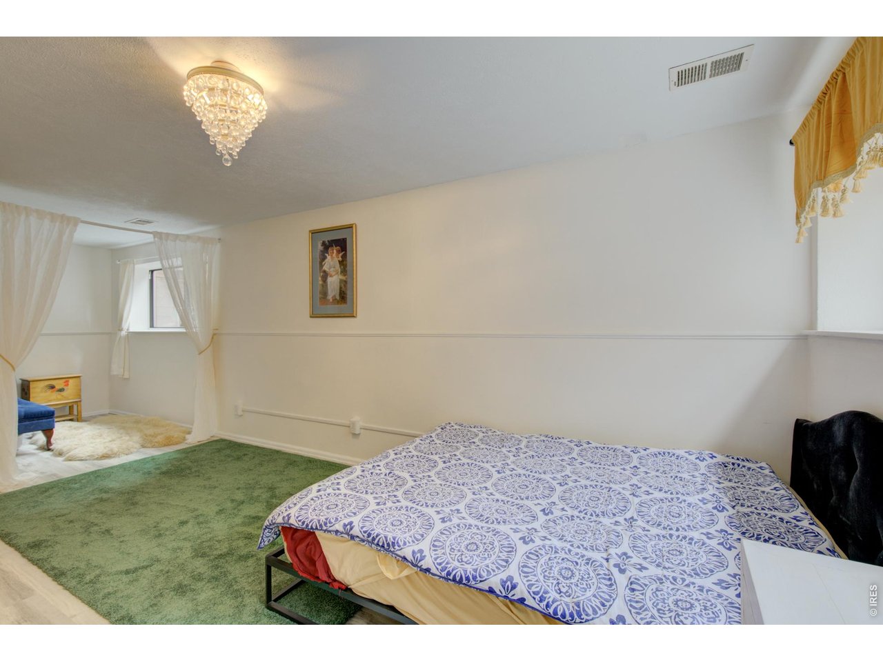 Furnished bedroom with a patterned bedspread, green carpet, and adjoining sitting area.