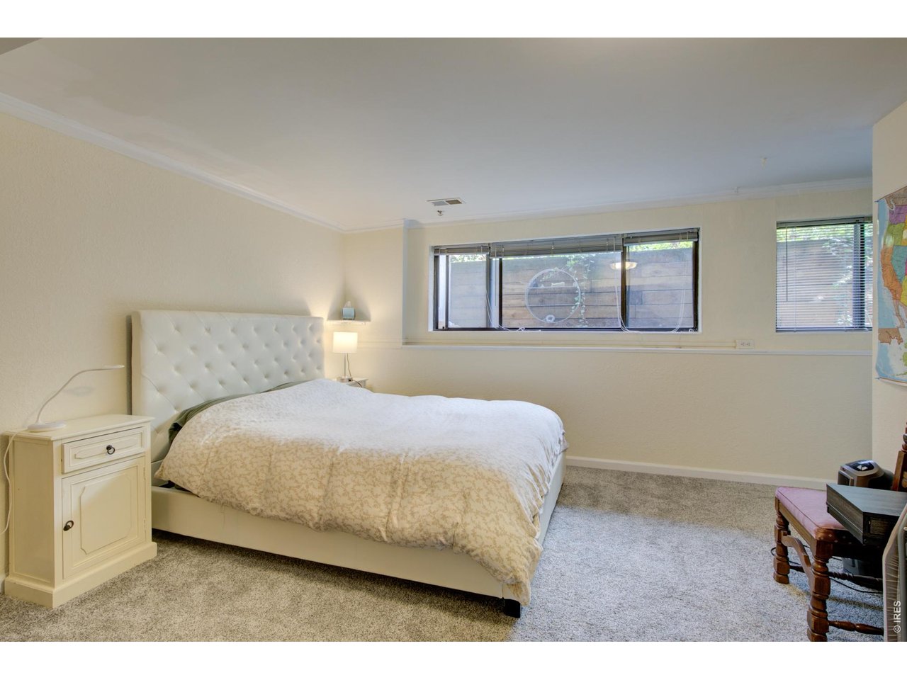 Furnished bedroom with a large bed, tufted white headboard, and windows overlooking a wooden fence.