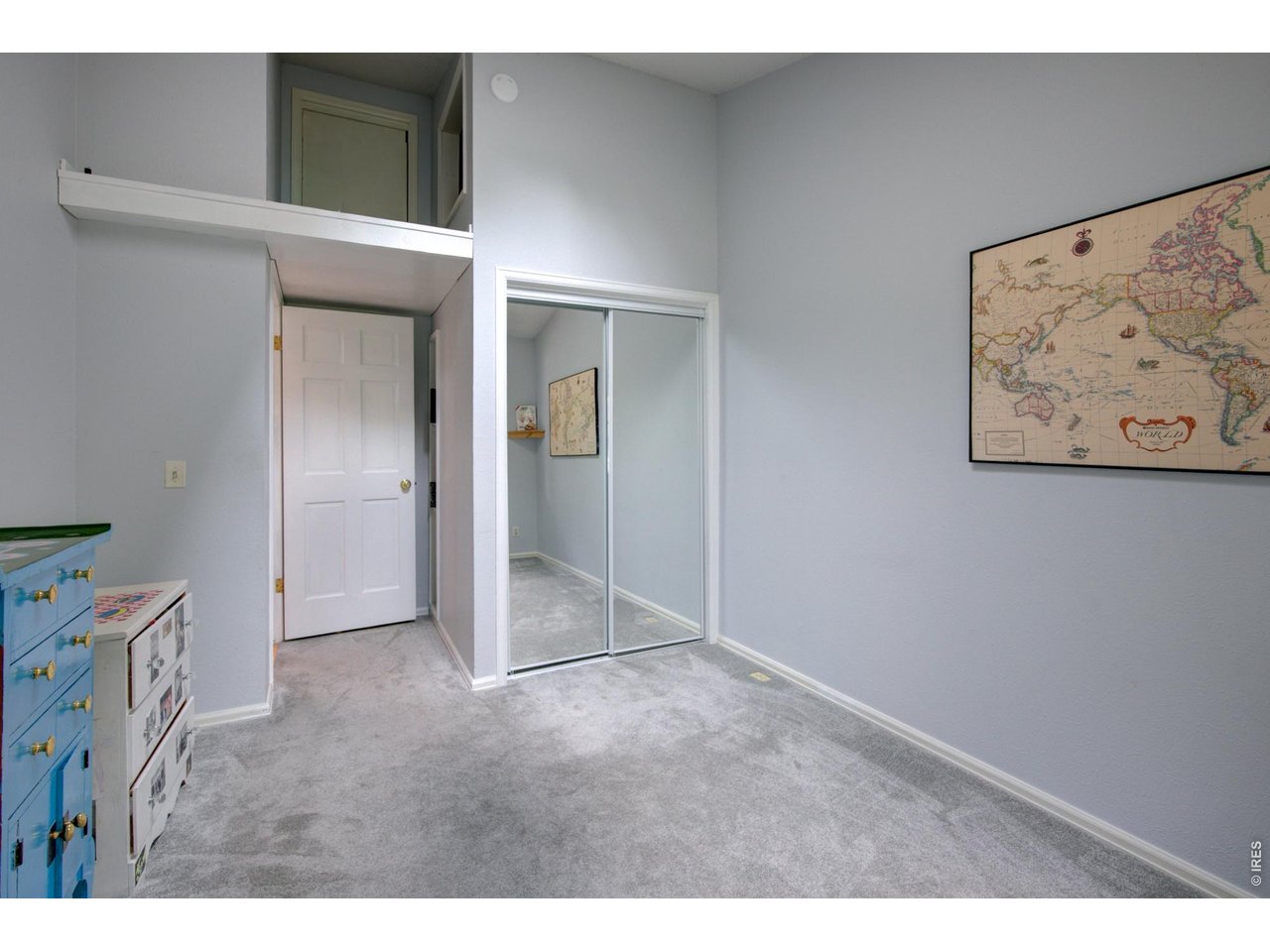 Carpeted bedroom with mirrored closet doors, colorful dressers, and a framed world map.