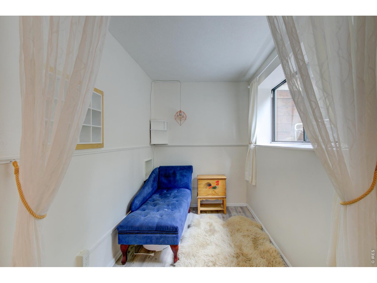 Sitting room with a blue chaise lounge, shag rug, and sheer curtains around a window.