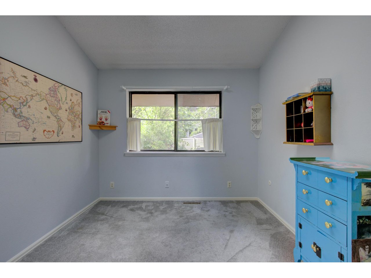 Bedroom with gray carpet, a window overlooking greenery, a wall map, and a bright blue dresser.