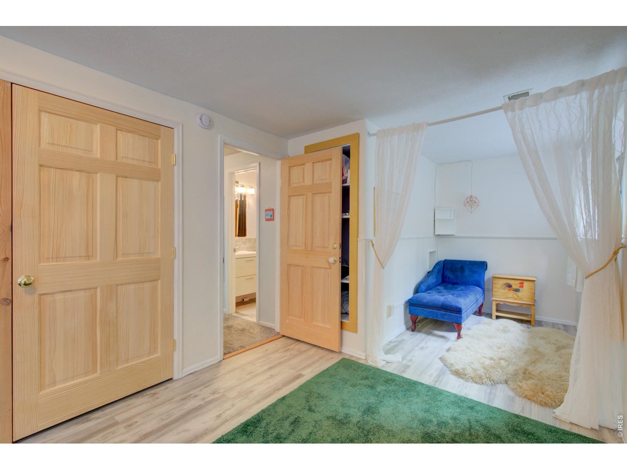 Furnished room with a blue chaise lounge, sheer curtains, and light wood doors.