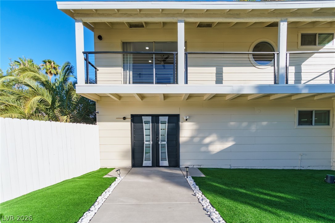 Two-story house entry with a covered balcony, modern double doors, and a stone-edged walkway.
