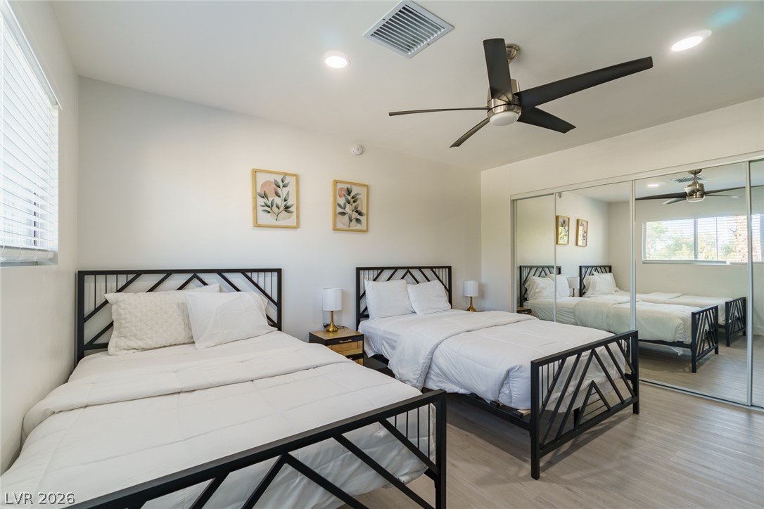 Bedroom with two white-dressed beds, black metal frames, mirrored closet doors, and a ceiling fan.