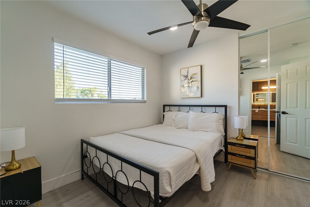 Bedroom with a black metal bed, white bedding, mirrored closet doors, and a wide window with blinds.