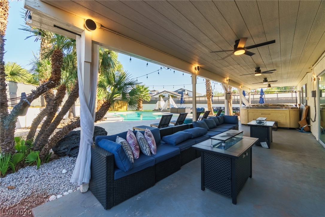 Covered patio with blue lounge seating overlooks a backyard pool and hot tub.