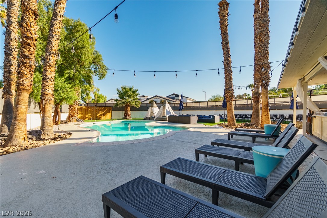 Backyard pool bordered by palm trees, with lounge chairs and overhead string lights.