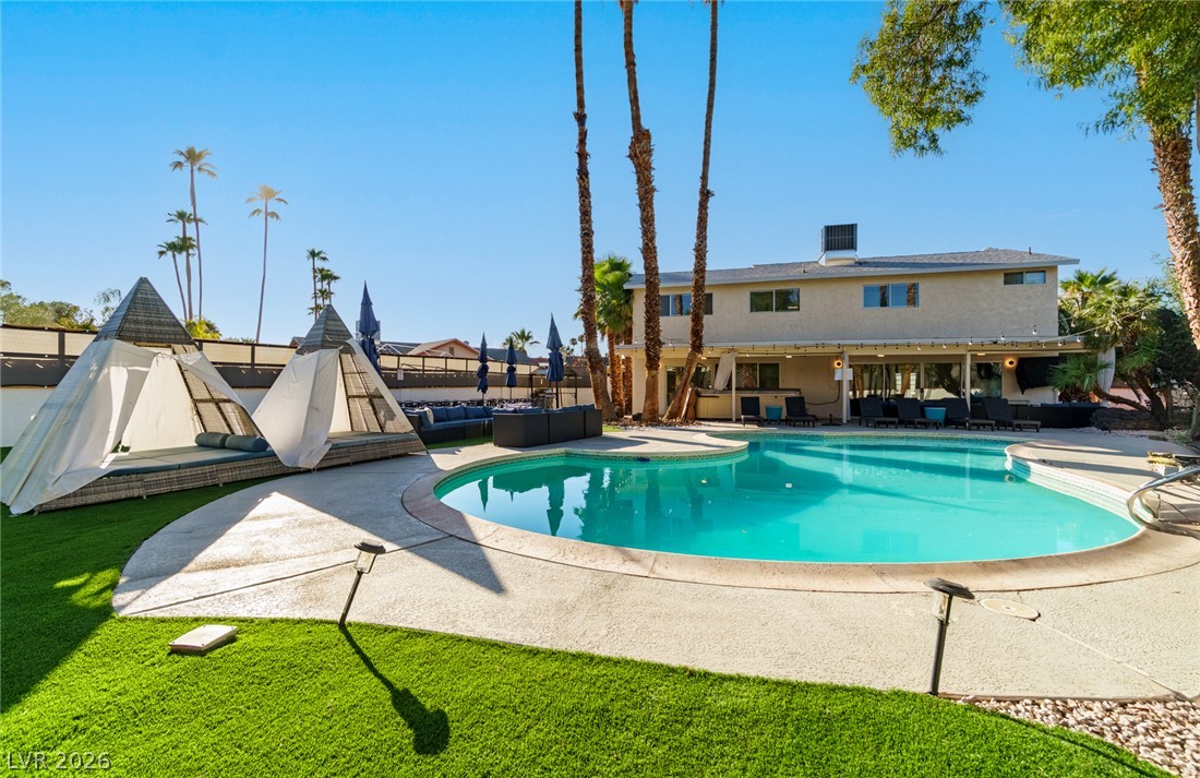 Backyard pool beside a two-story house, with pyramid cabanas and outdoor seating.