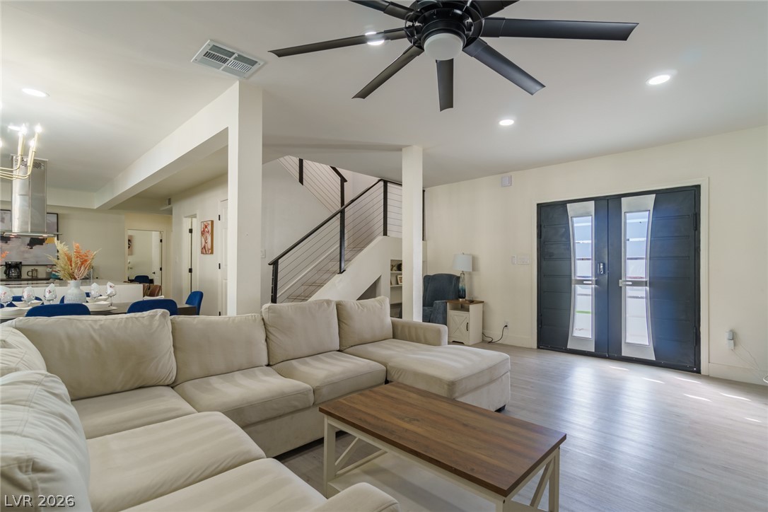 Open-plan living room with a cream sectional, wood coffee table, and modern dark double doors.