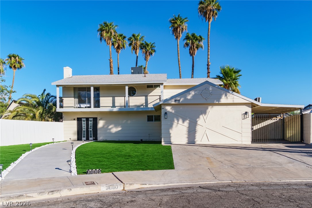 Two-story home with a broad garage, covered carport, curved driveway, and palm trees.