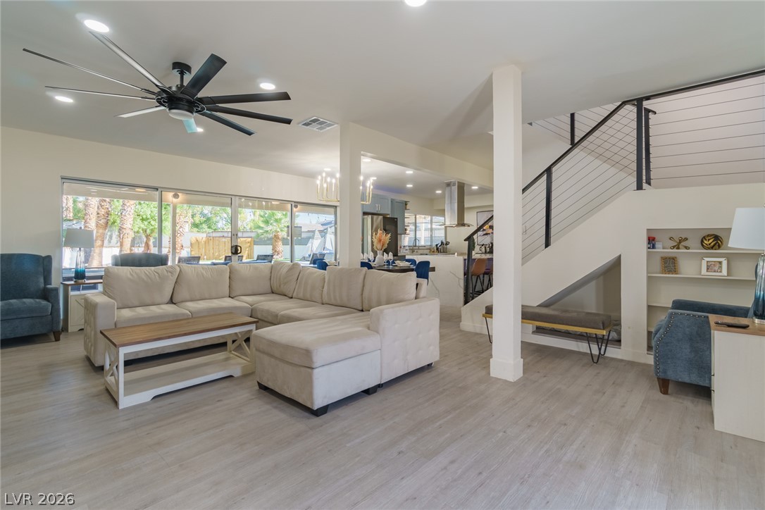 Open-plan living room with a white sectional, large garden-facing windows, and a cable-railed staircase.