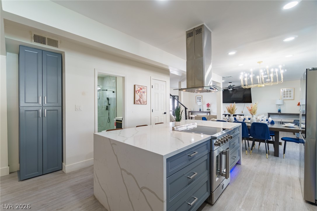 Kitchen with a large veined quartz island, blue-gray cabinets, and an open dining area with blue chairs.